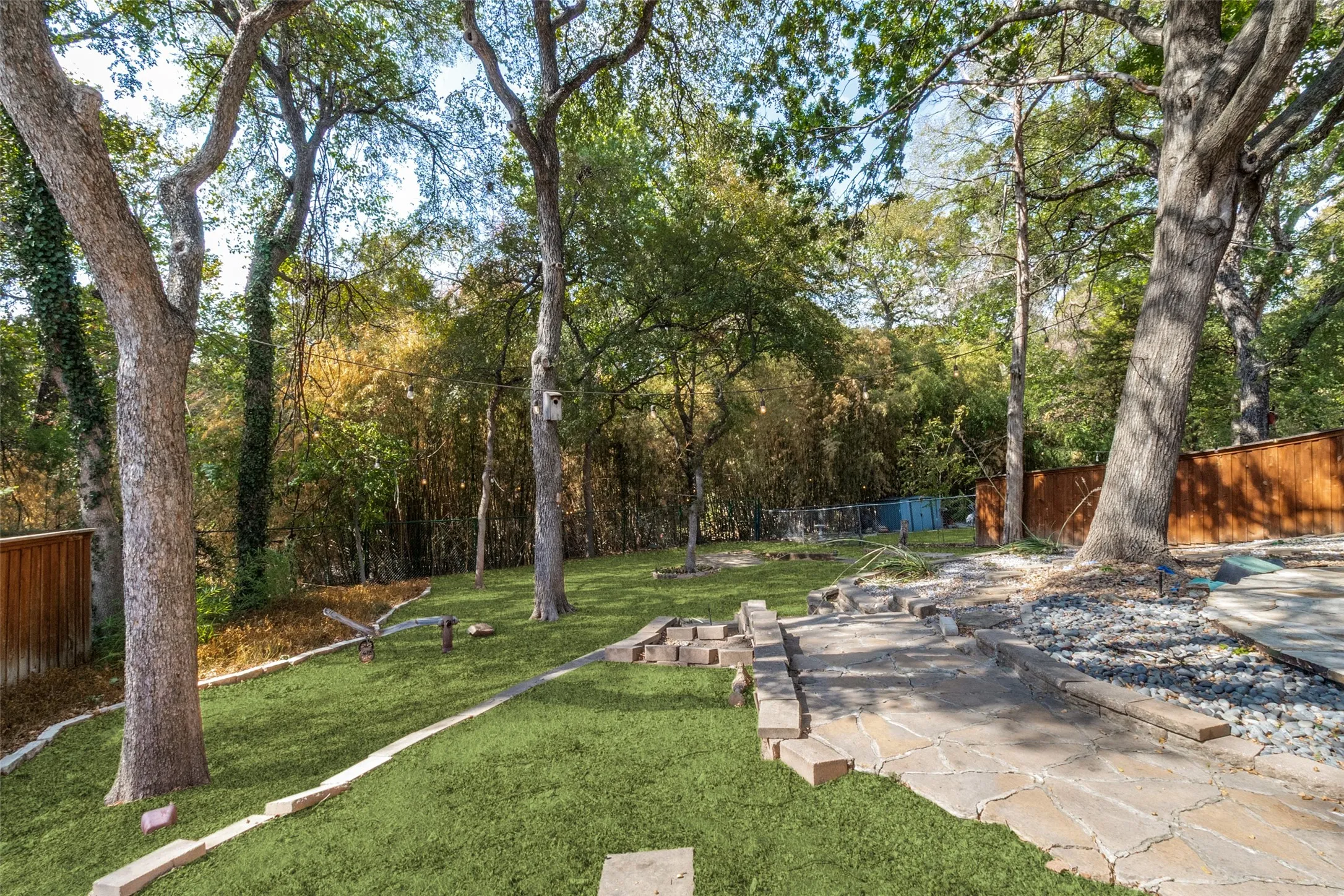 Expansive yard featuring mature trees, artificial turf, and a natural stone pathway