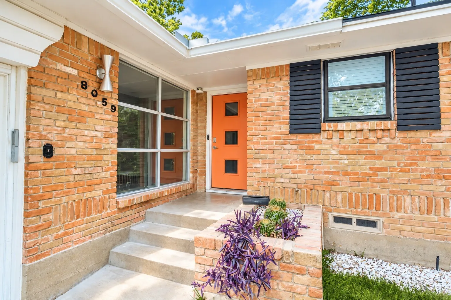 Digitally enhanced - Brick facade with a vibrant orange entry door, concrete steps, and integrated planter box