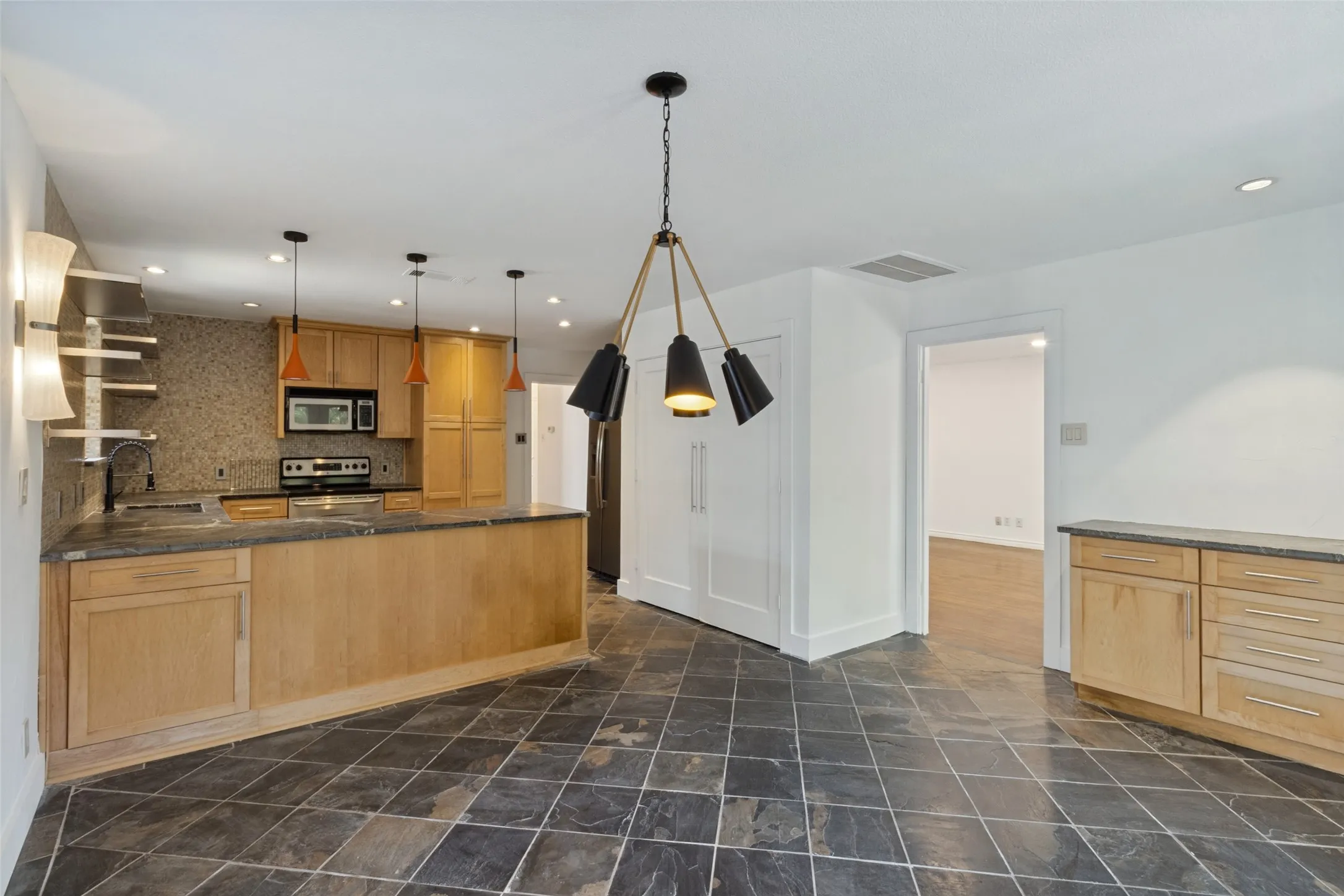 Kitchen with light wood cabinetry, stone countertops, integrated microwave, and a tile backsplash