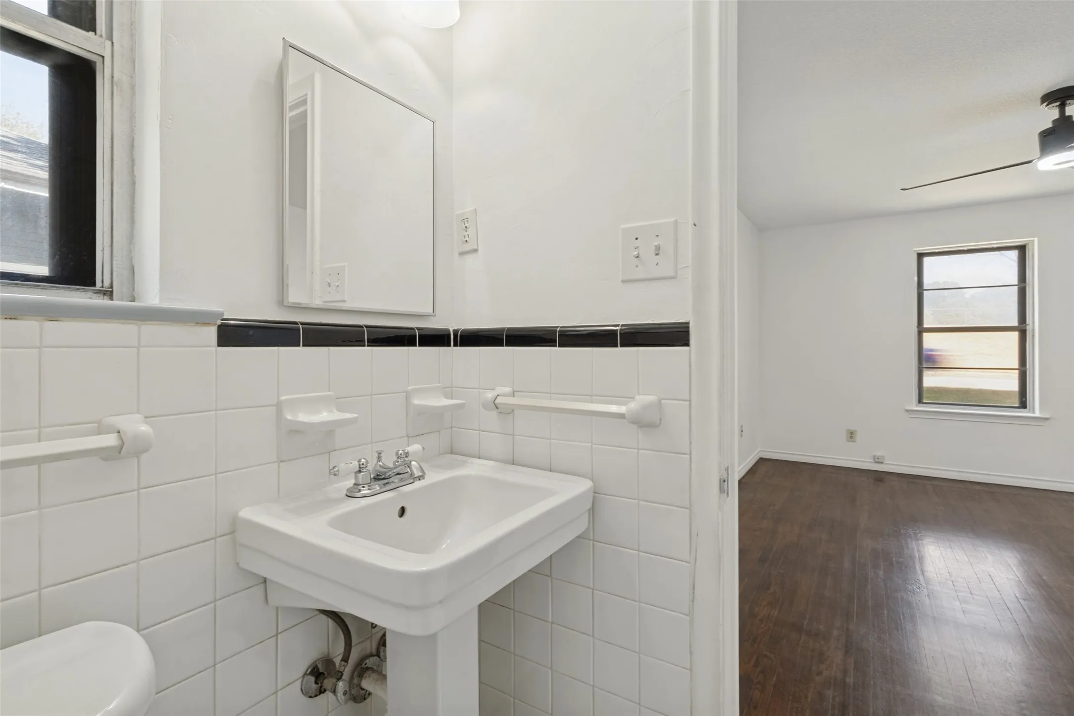 Pedestal sink with chrome fixtures and white tiled walls with a black accent border