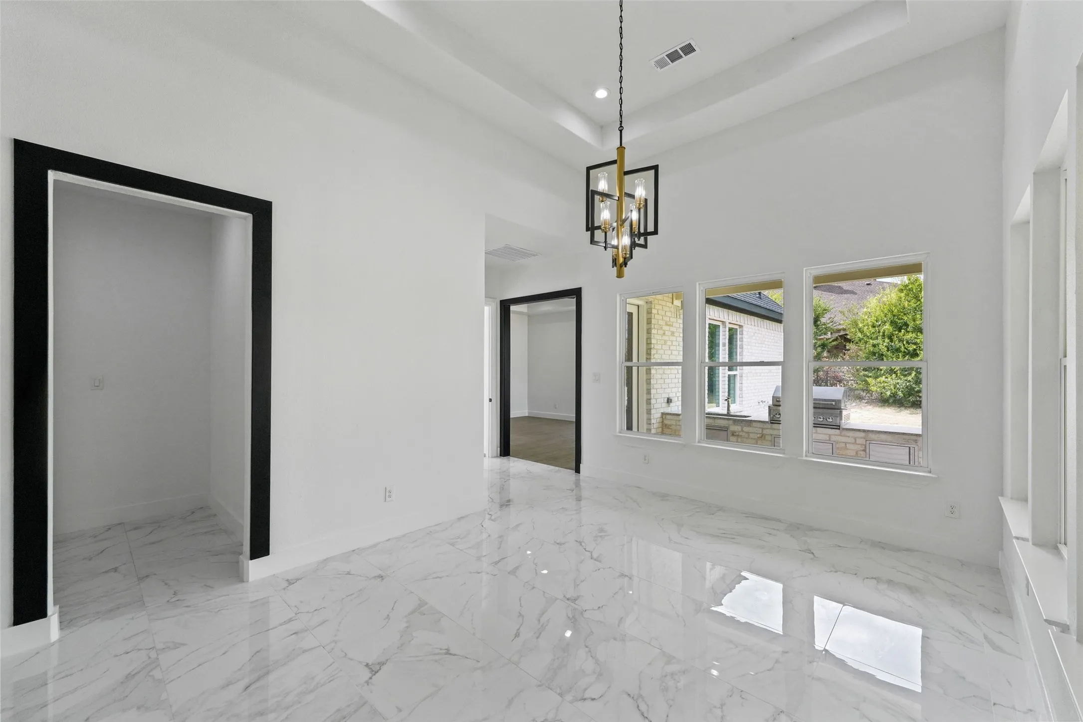Vaulted ceiling with an elegant hanging chandelier, white walls, large windows, and gloss-finish tile flooring