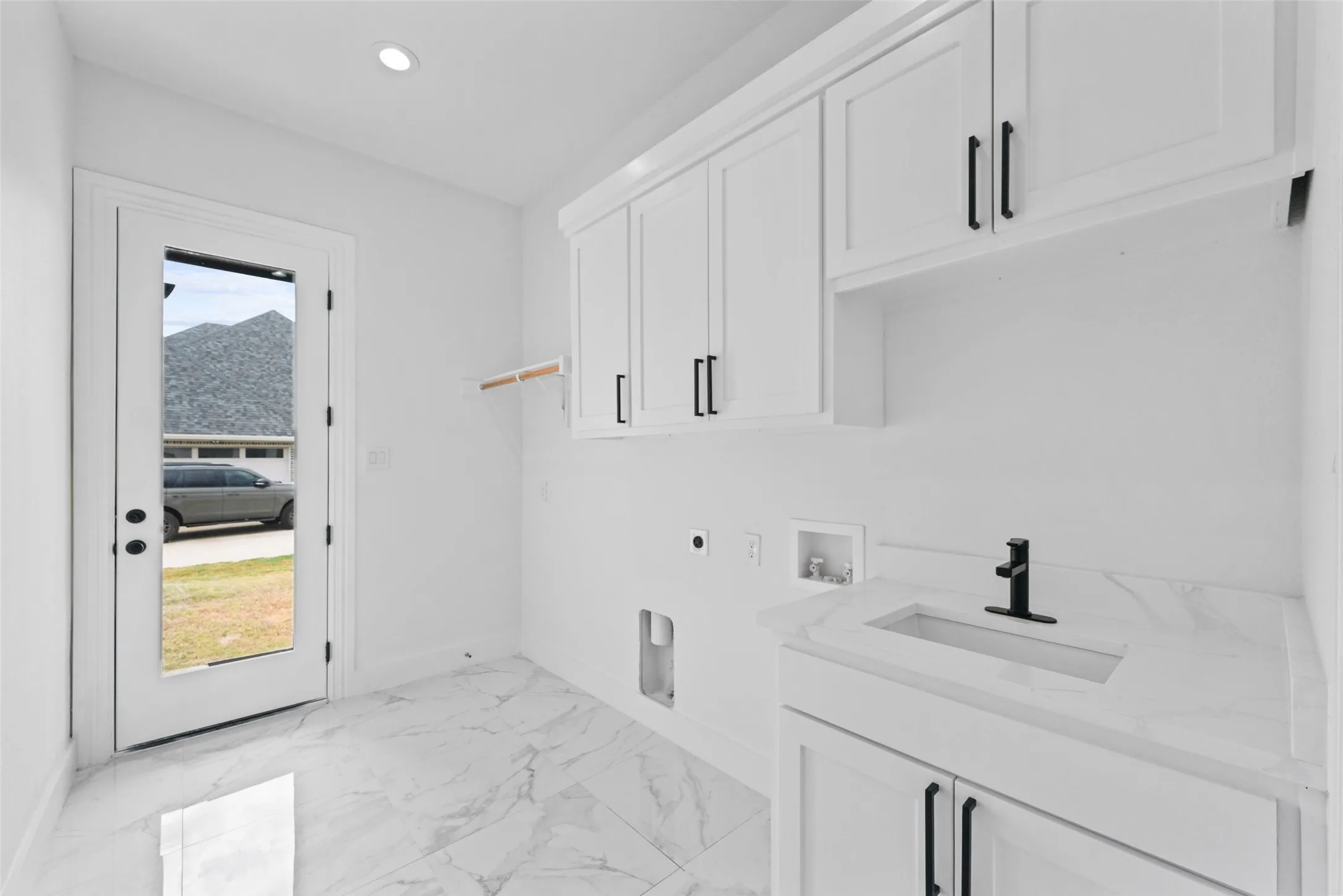 White cabinetry with matte black hardware, recessed lighting, wood-finish shelving, and a vanity with an integrated sink