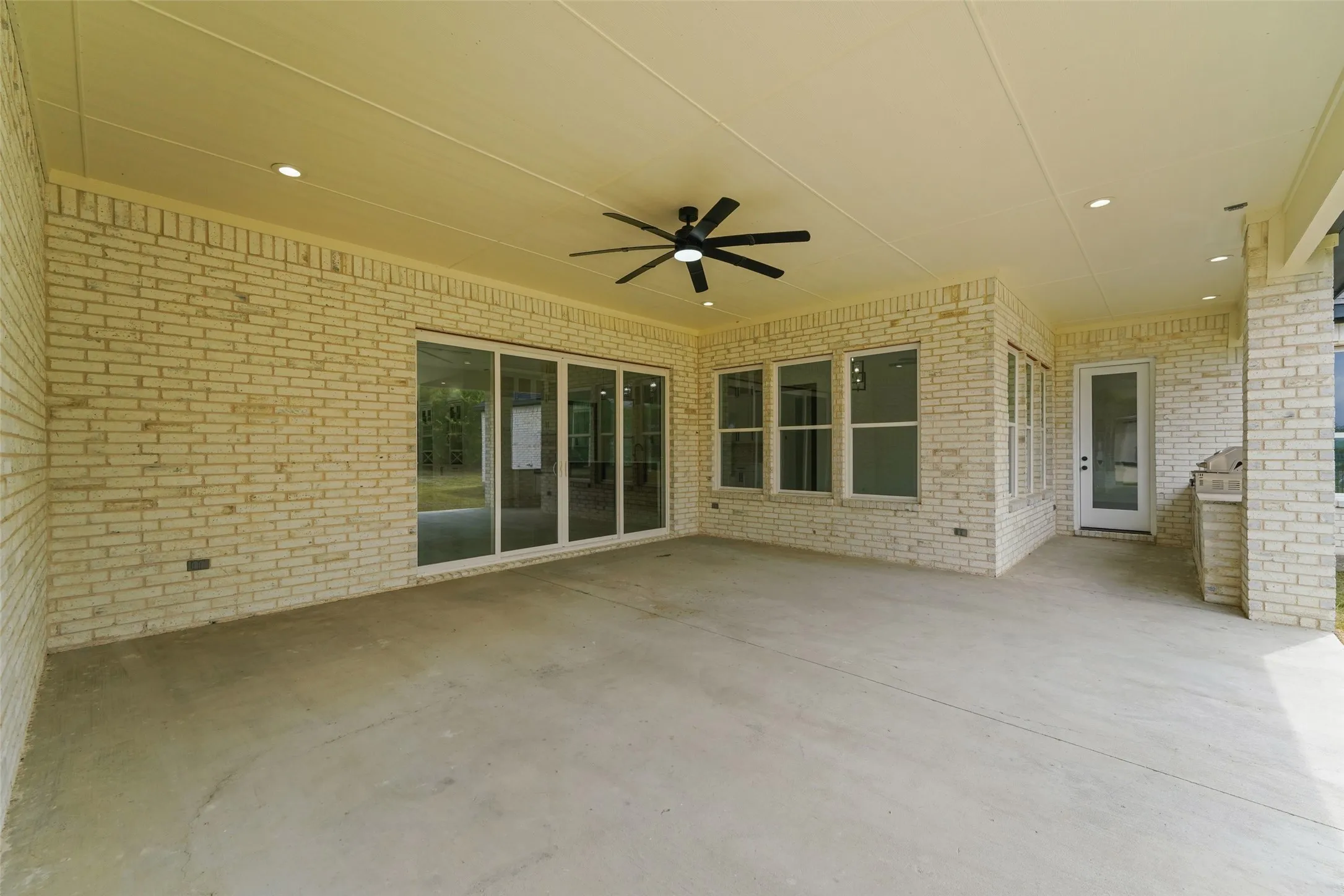 Expansive covered patio featuring a concrete surface, white brick exterior, ceiling fan, and recessed lighting