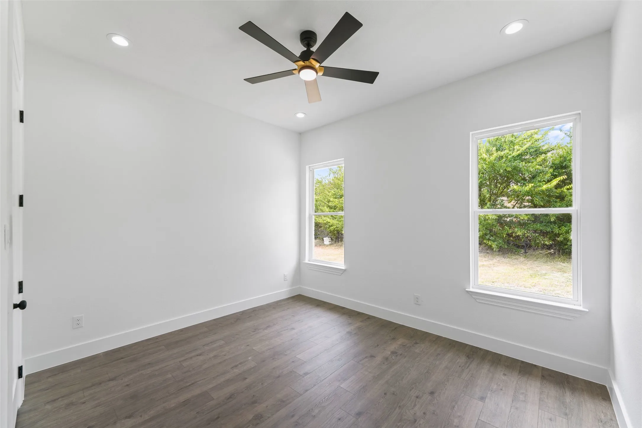 Recessed lighting, wood-finish flooring, two window units, and a ceiling fan with integrated lighting