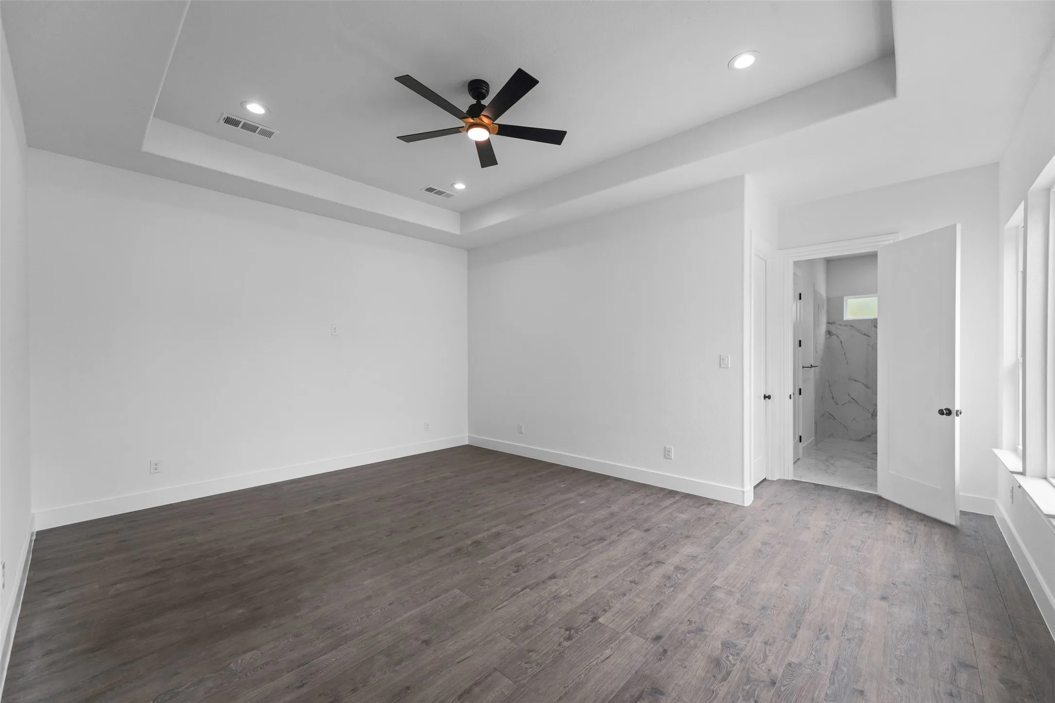 Spacious room featuring wood-finish flooring, a tray ceiling with recessed lighting, and a ceiling fan