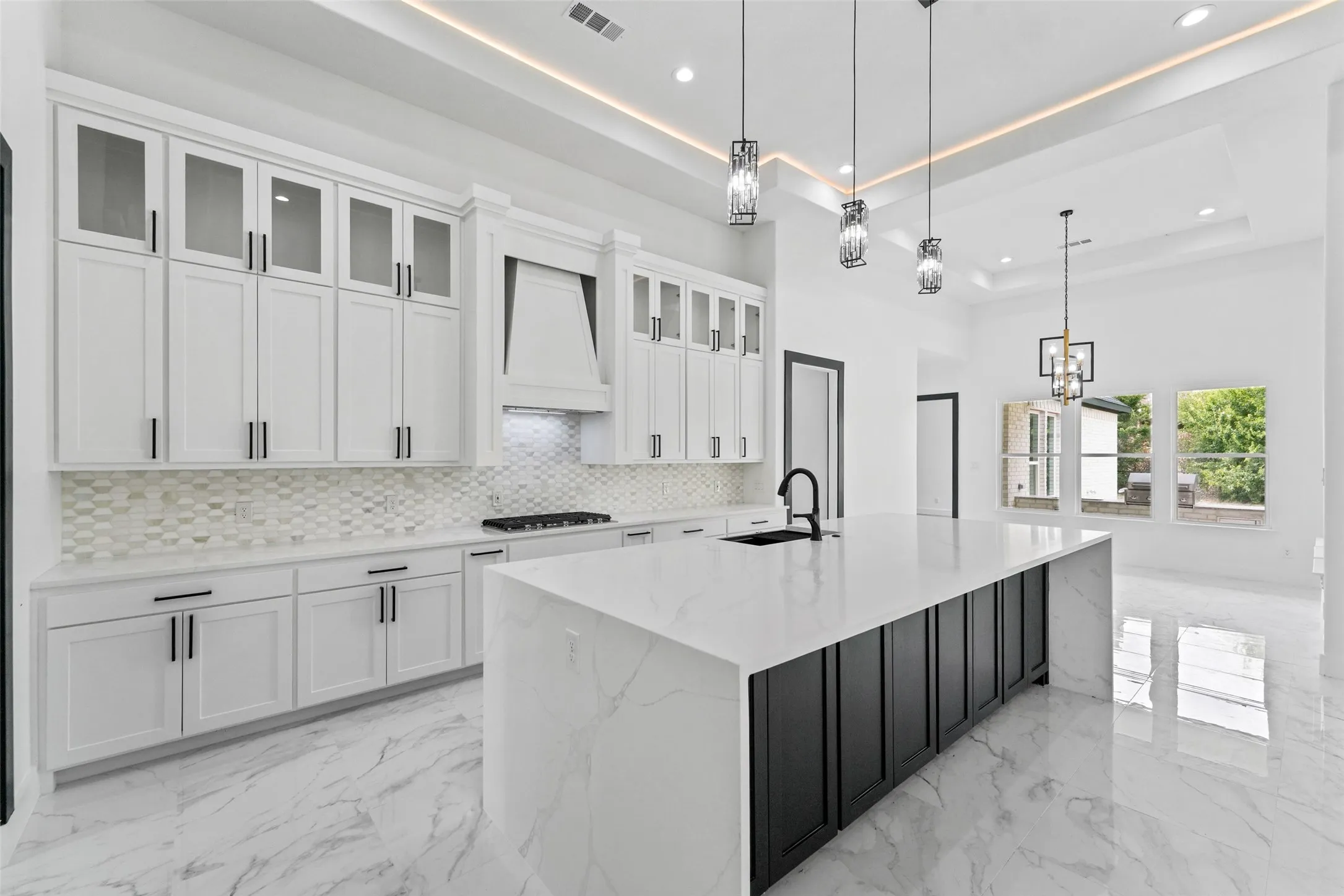 White cabinetry with black hardware, a large kitchen island with a waterfall countertop, mosaic tile backsplash, recessed lighting, and decorative pendant lights