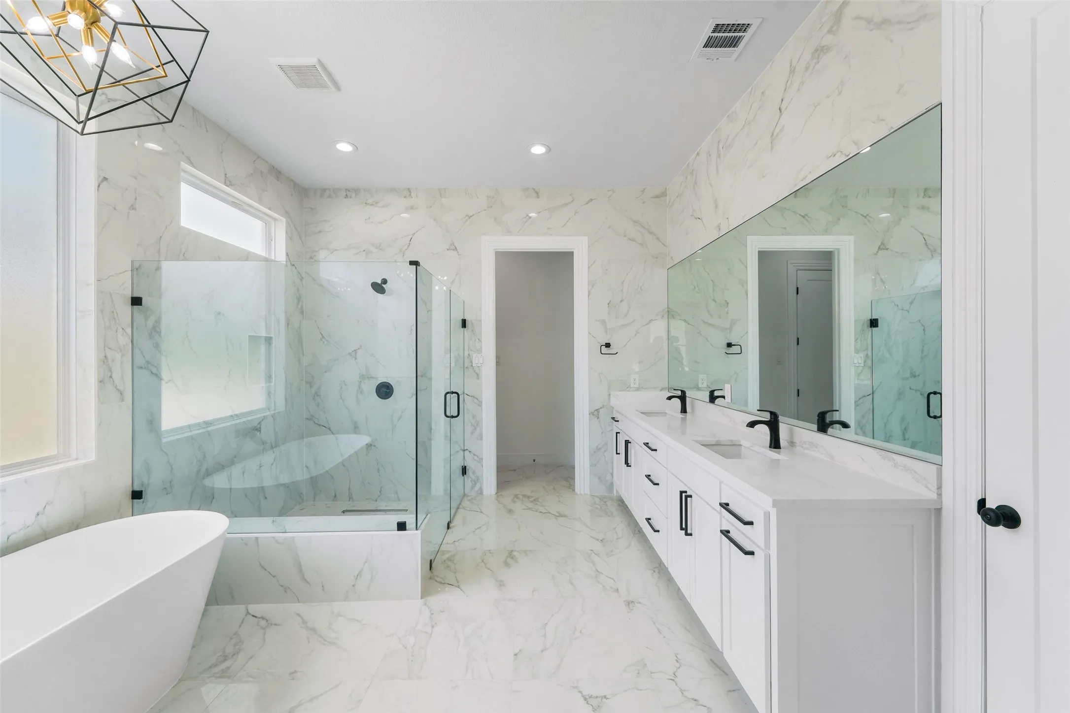 Spacious bathroom featuring a freestanding tub, glass-enclosed shower, dual vanity with white cabinetry, and large format marble-look tile