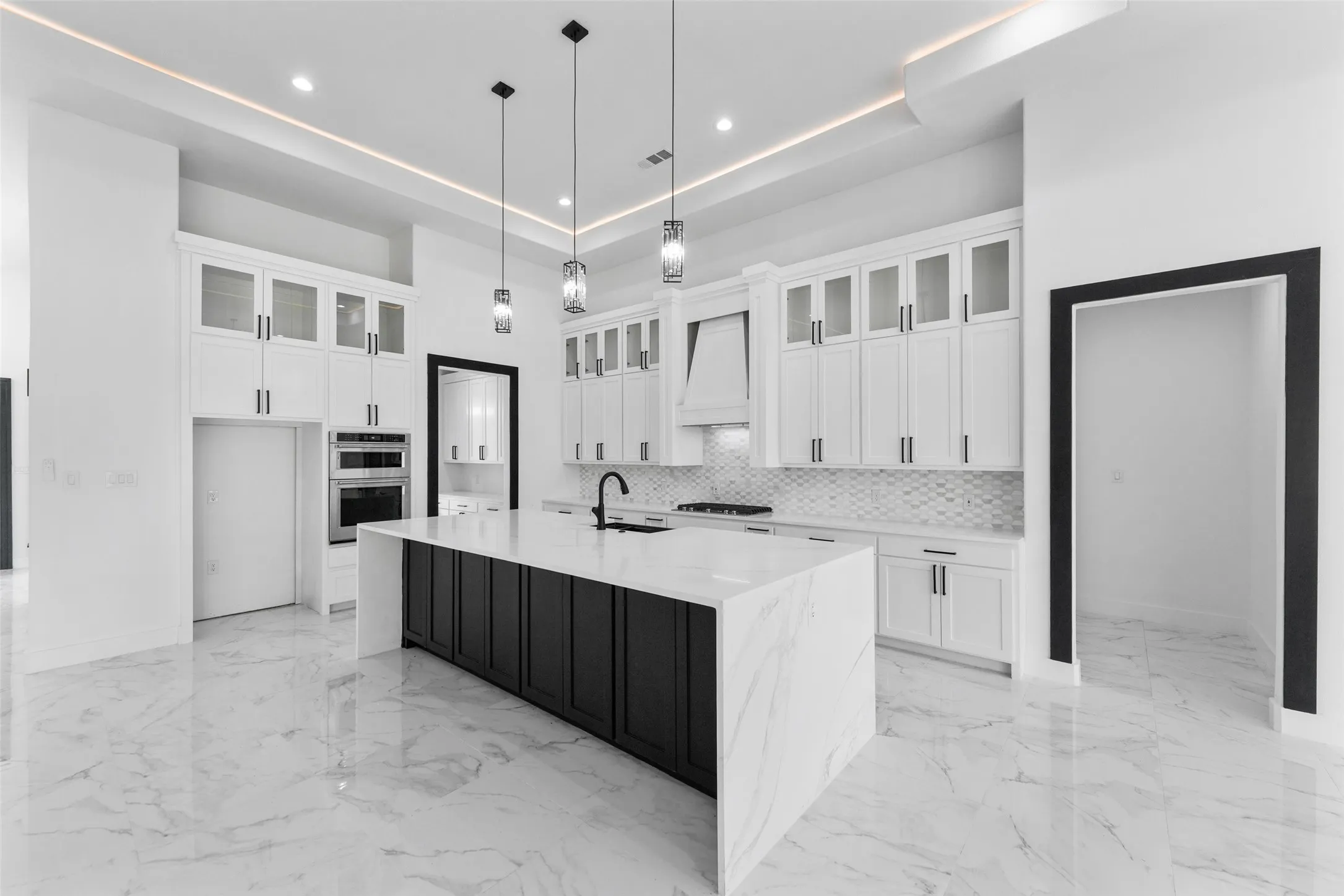 Open-concept kitchen featuring a waterfall island with a dark base, white cabinetry, integrated stainless steel appliances, and large format marble-look tile flooring