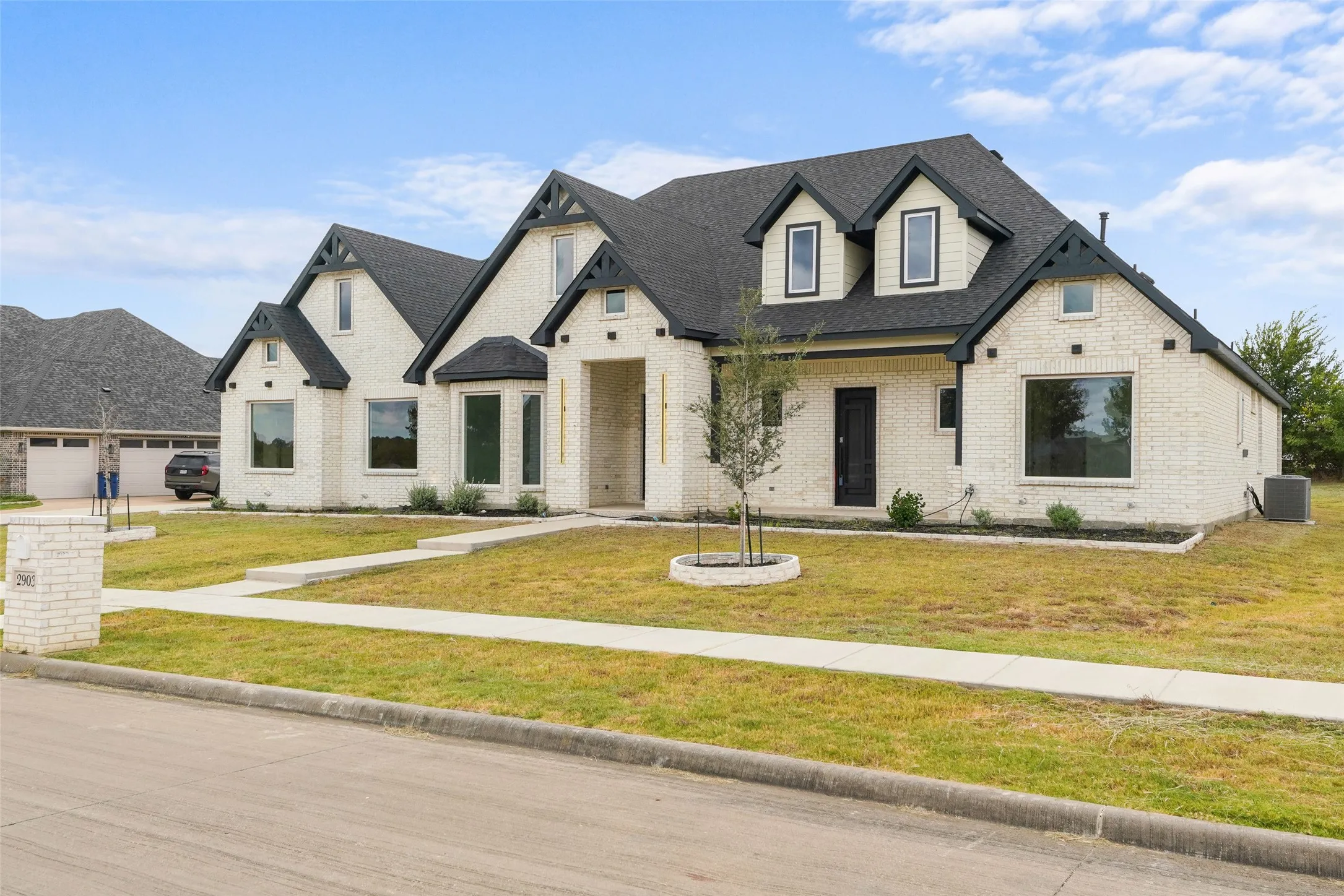 White brick exterior with dark trim accents, a prominent front entry, multiple gabled rooflines, and a well-defined front walkway