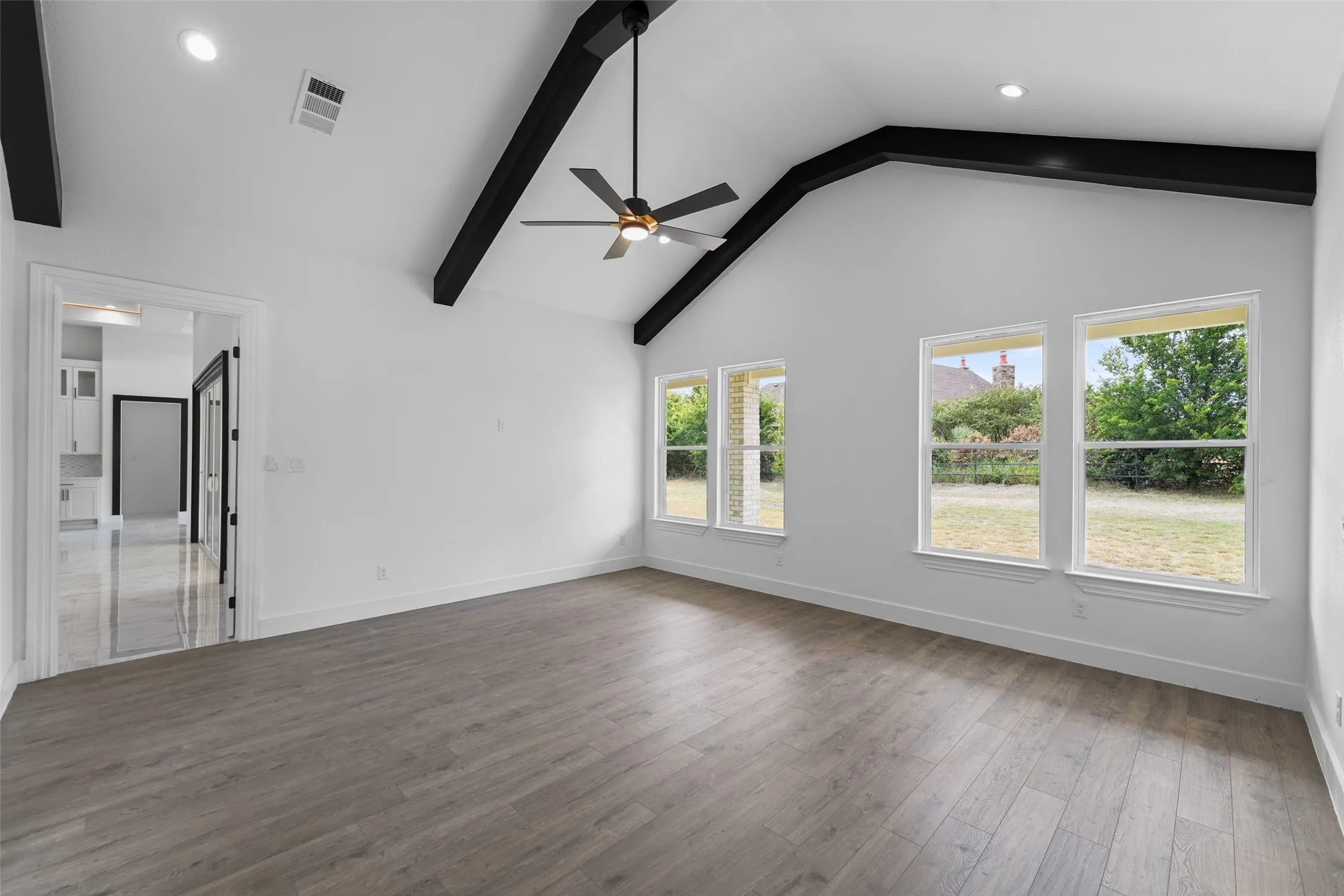 Vaulted ceiling with exposed black beams, wood-finish flooring, recessed lighting, and multiple windows