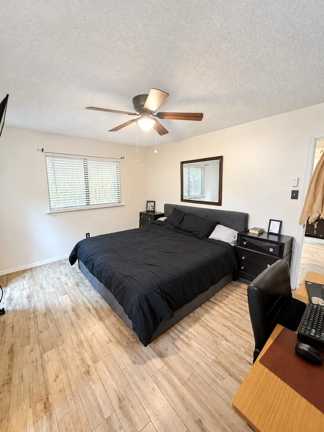 Wood-finish flooring, ceiling fan with integrated lighting, window with blinds, wall-mounted mirror, and a built-in wall niche