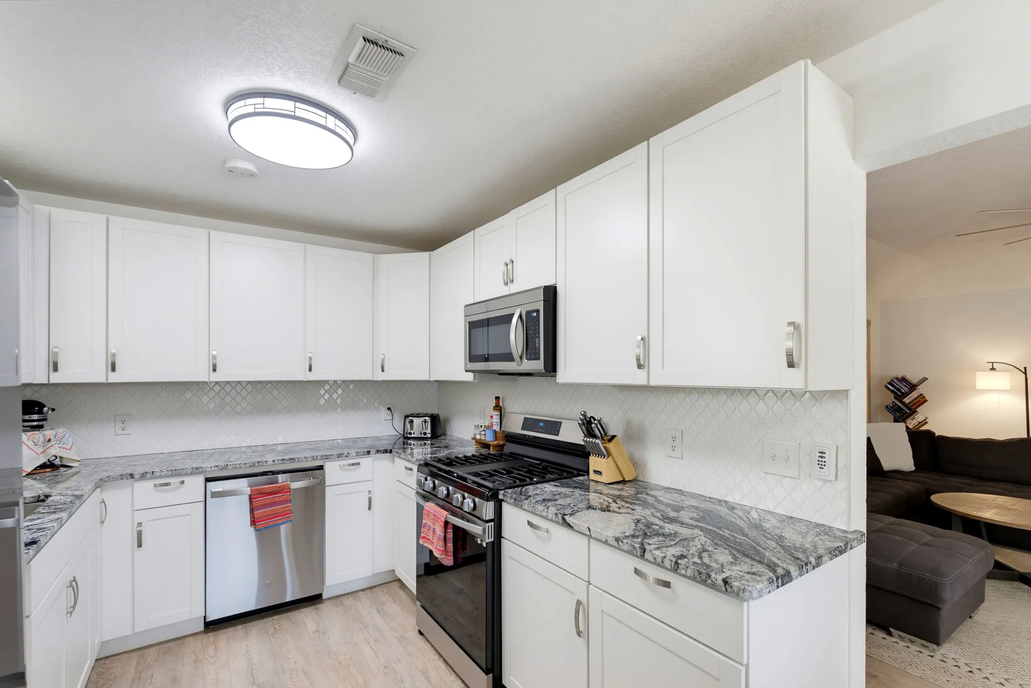 Modern kitchen featuring white shaker-style cabinetry, stainless steel appliances, speckled countertops, and a patterned tile backsplash
