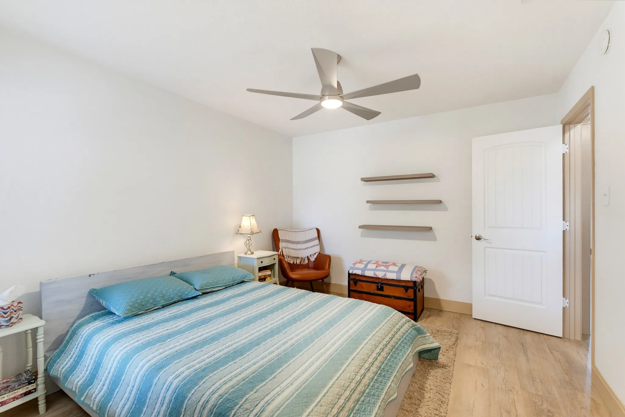 Wood-finish flooring with white baseboards, a ceiling fan with integrated lighting, and a white paneled door