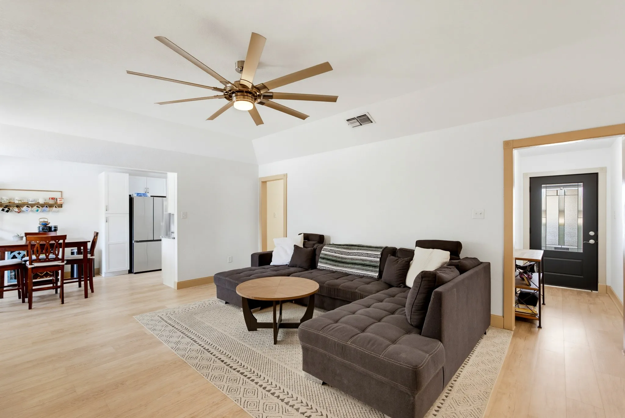 Vaulted ceiling with an expansive ceiling fan, light wood-finish flooring, white walls, and a black entry door with decorative glass inserts