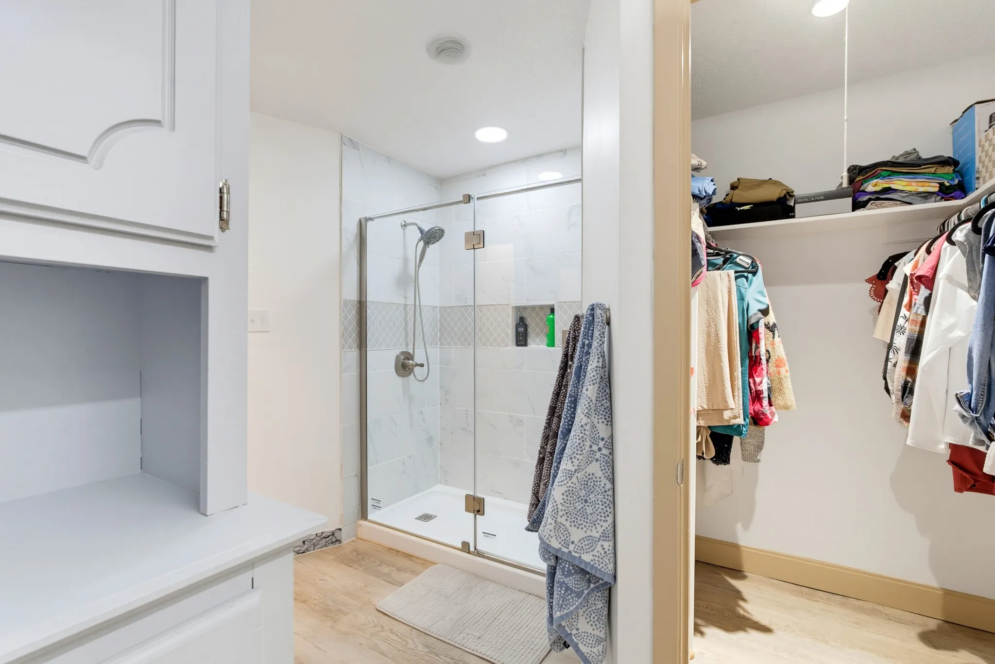 Enclosed shower with glass door and tile surround, recessed lighting, wood-finish flooring, and built-in shelving