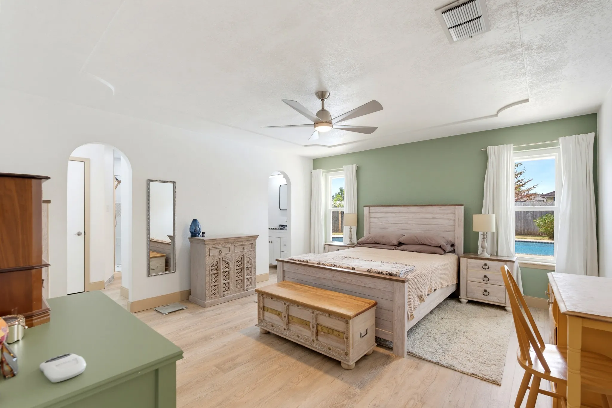Wood-finish flooring, ceiling fan, arched doorways, and windows with outdoor pool visibility