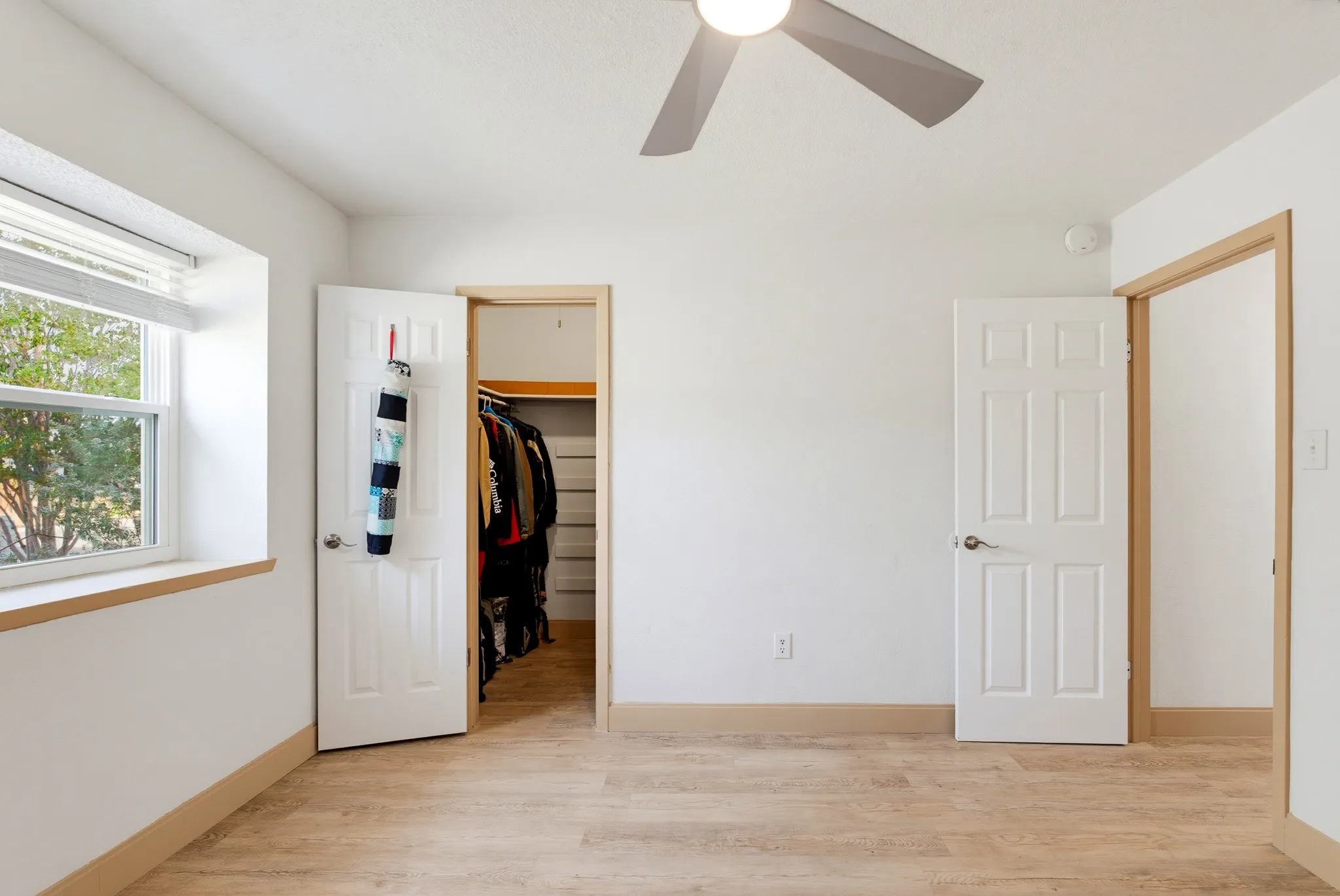 Recessed window with blinds, wood-finish flooring, ceiling fan, white paneled doors, and light-toned trim