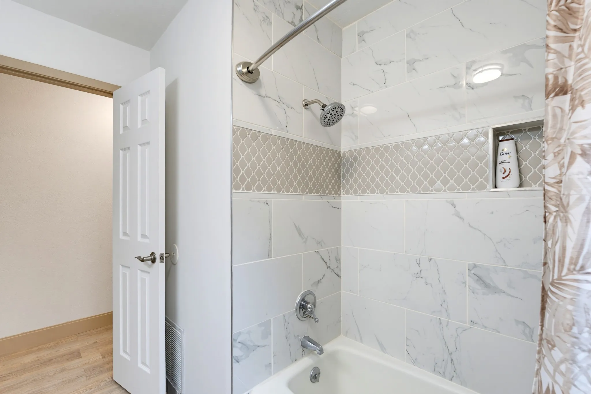 Bathtub and shower combination with white marble-style subway tile, decorative accent tile, and a recessed shower niche