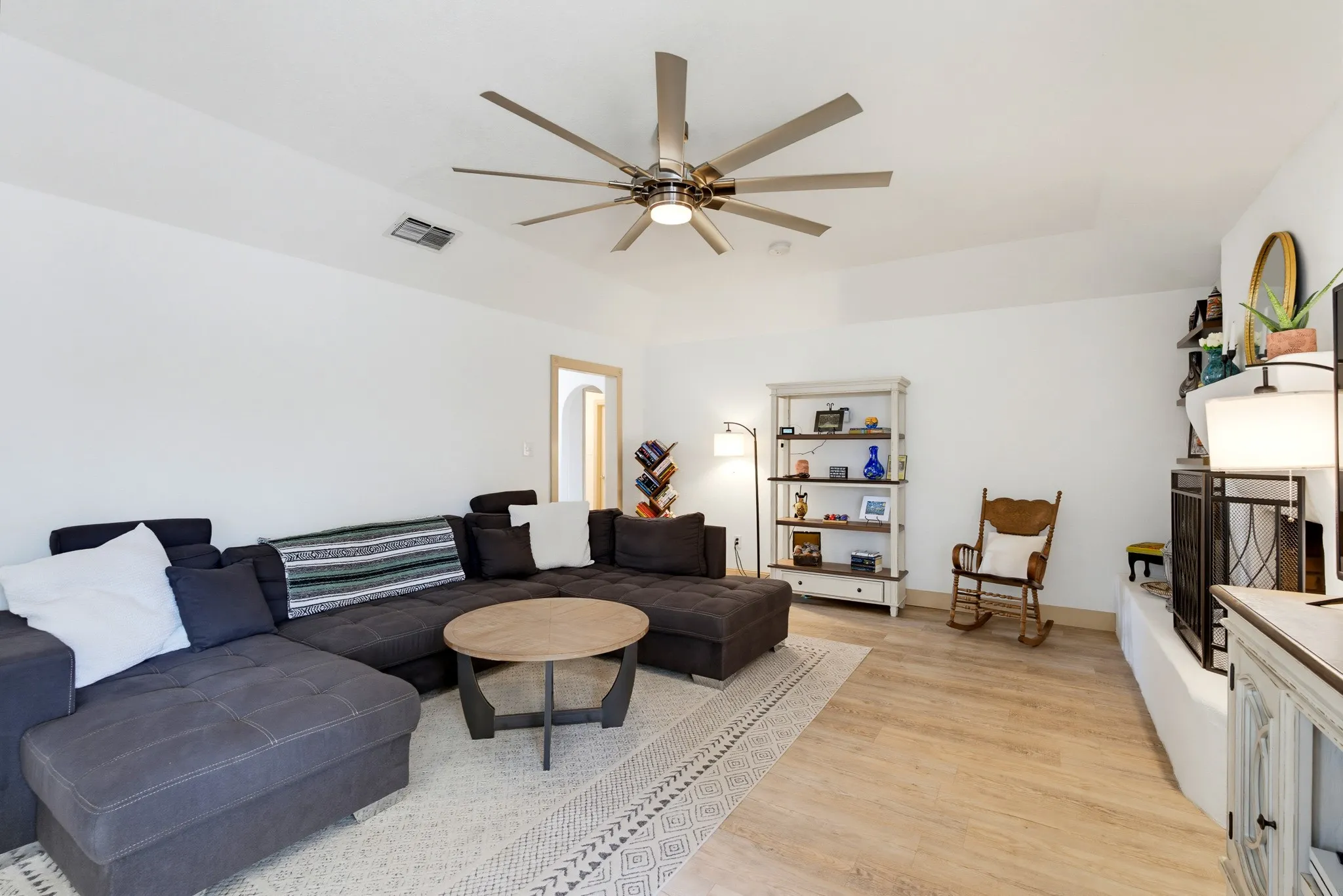 Spacious living area featuring light wood-finish flooring, a contemporary ceiling fan, and crisp white walls