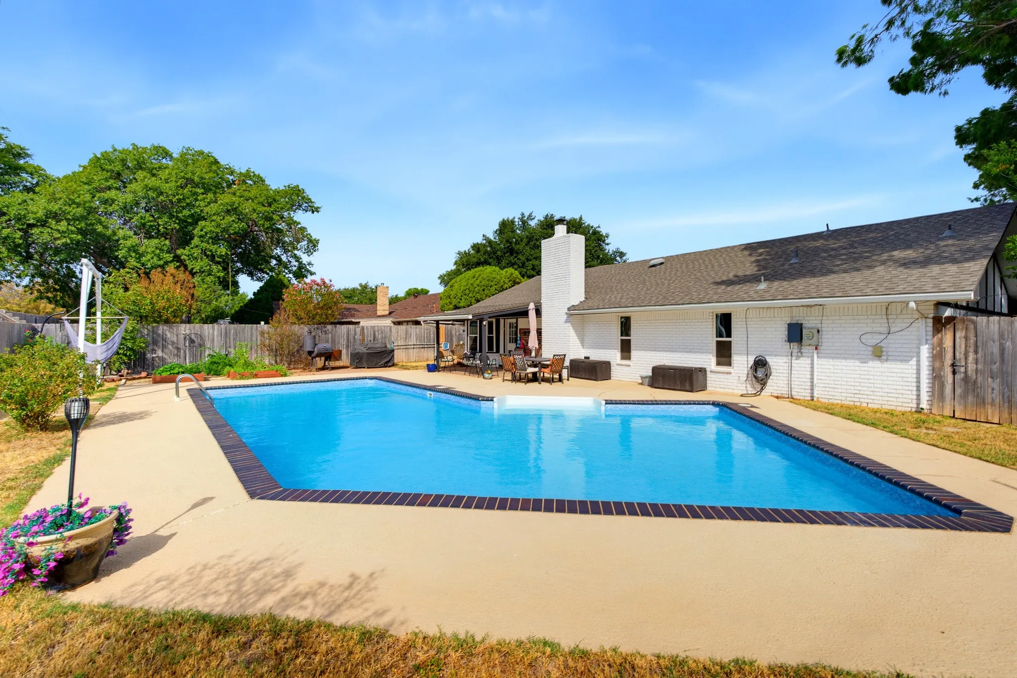 Backyard featuring an in-ground swimming pool, concrete patio, and a white brick exterior