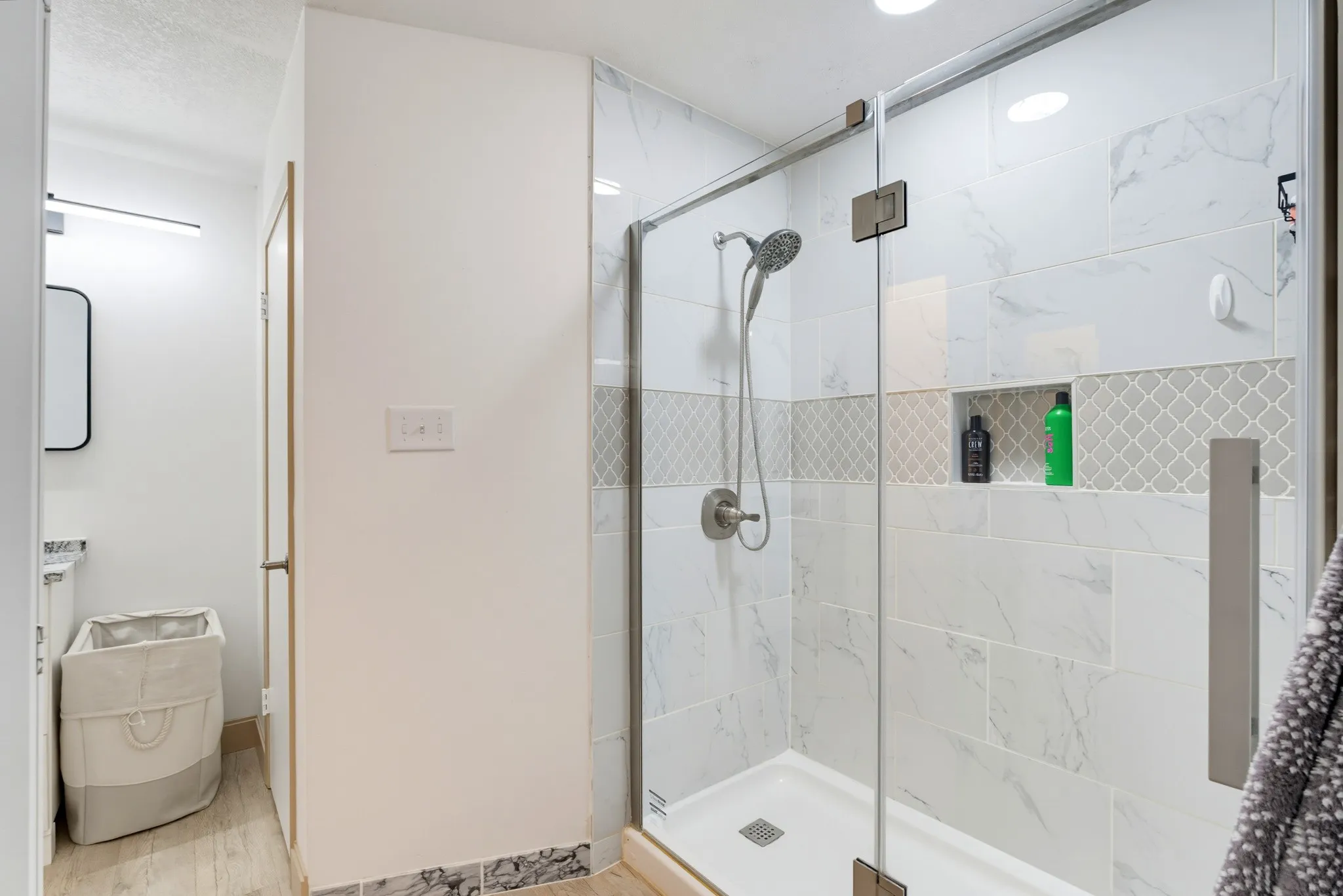 Glass-enclosed shower with a recessed shelf, white subway tile, decorative accent tile band, and brushed nickel fixtures