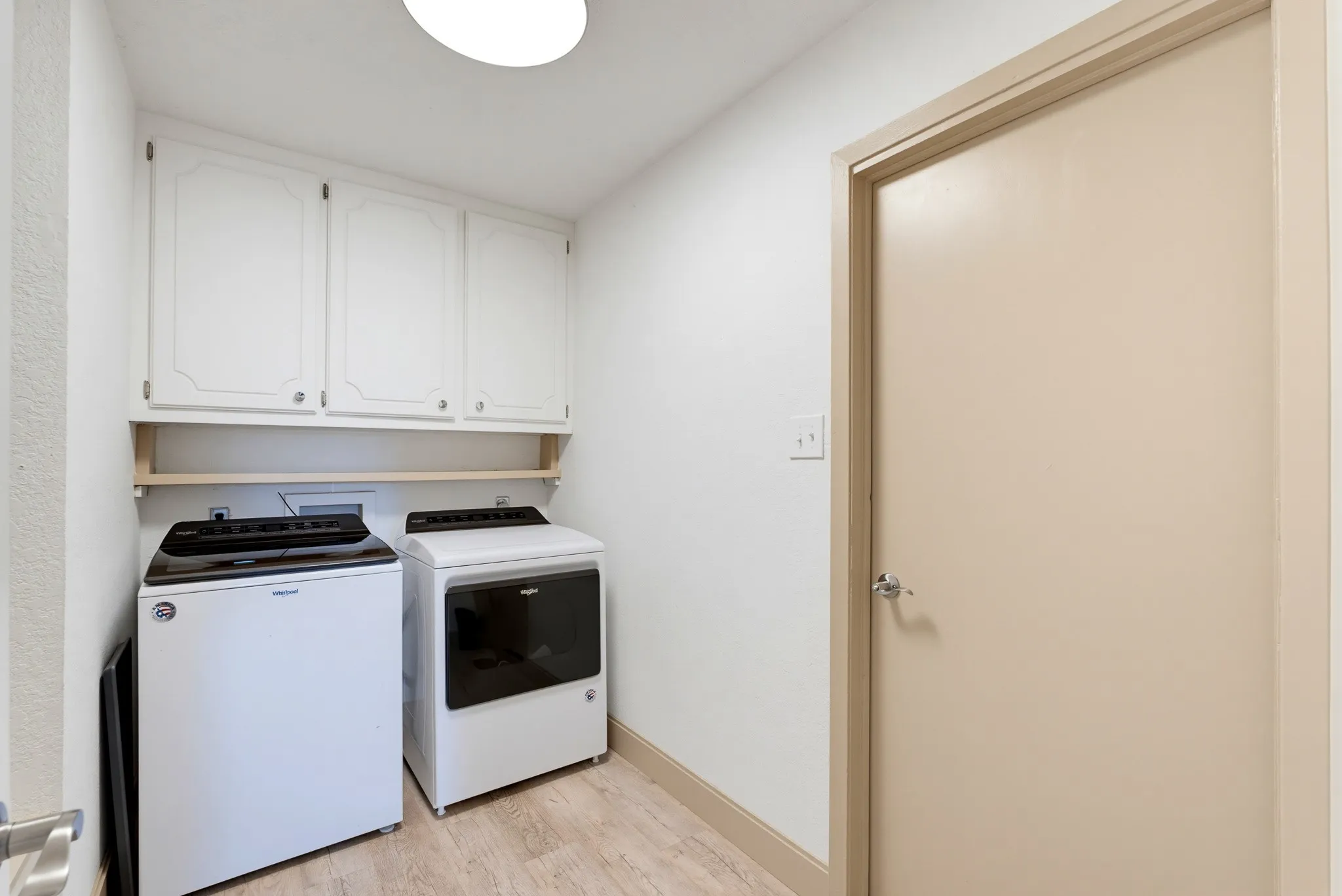 Upper cabinetry, light wood-finish flooring, and a flush-mount ceiling light