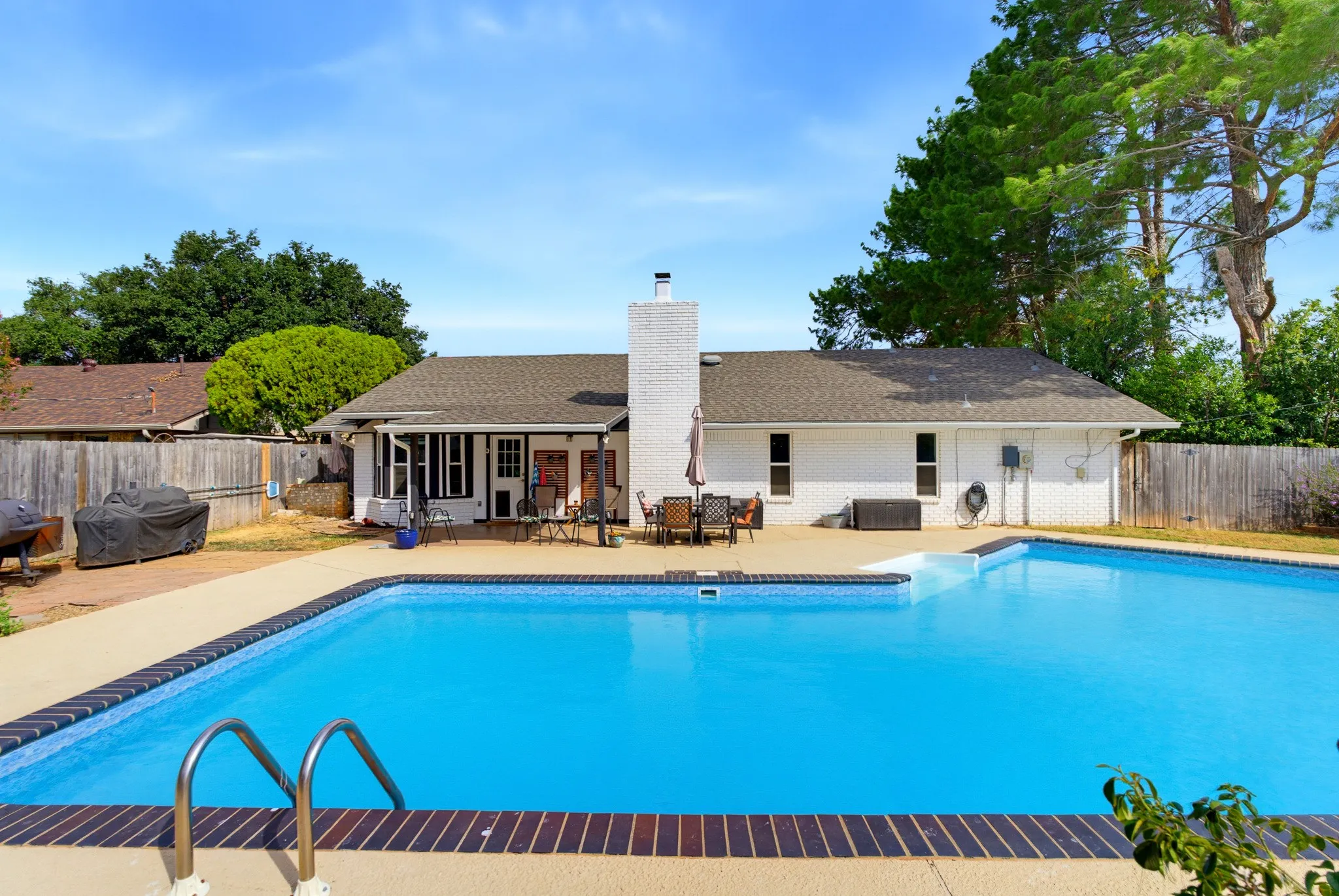 Backyard with a multi-level swimming pool, expansive concrete decking, and a covered patio area