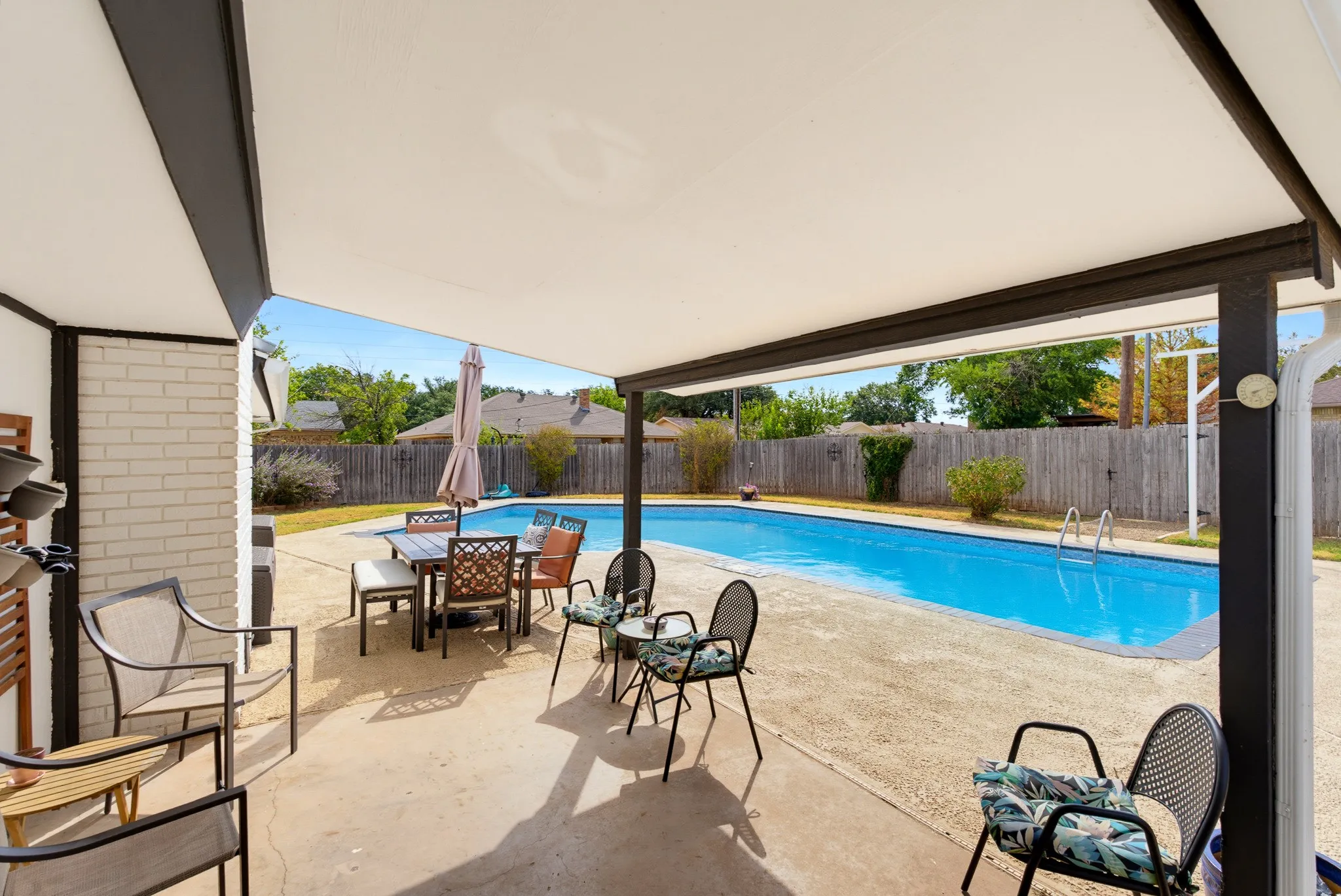 Expansive covered patio with concrete flooring, overlooking a rectangular inground swimming pool