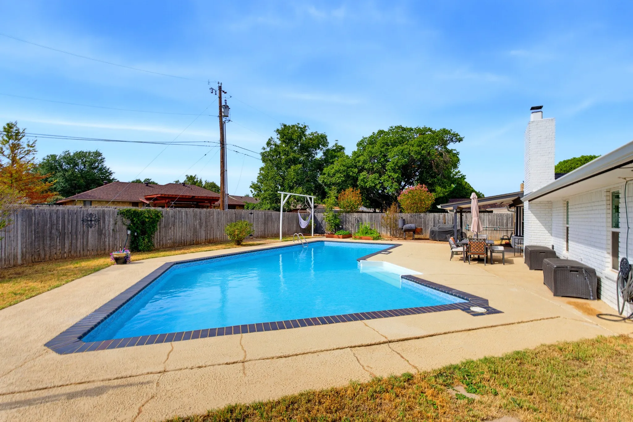 Rectangular swimming pool with integrated steps, concrete patio surround, and white brick exterior
