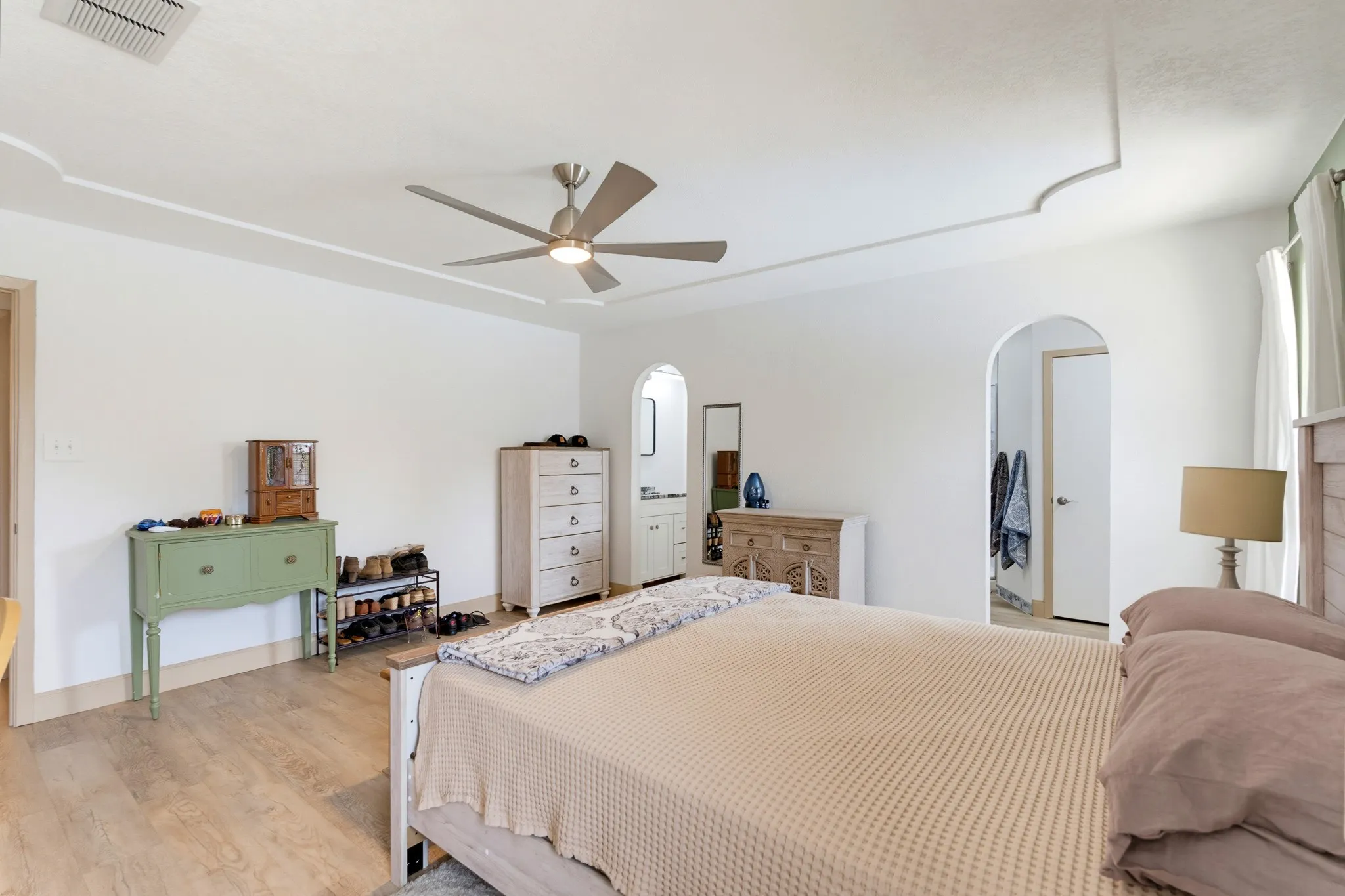 Wood-finish flooring, recessed ceiling with decorative trim, contemporary ceiling fan, and arched doorways