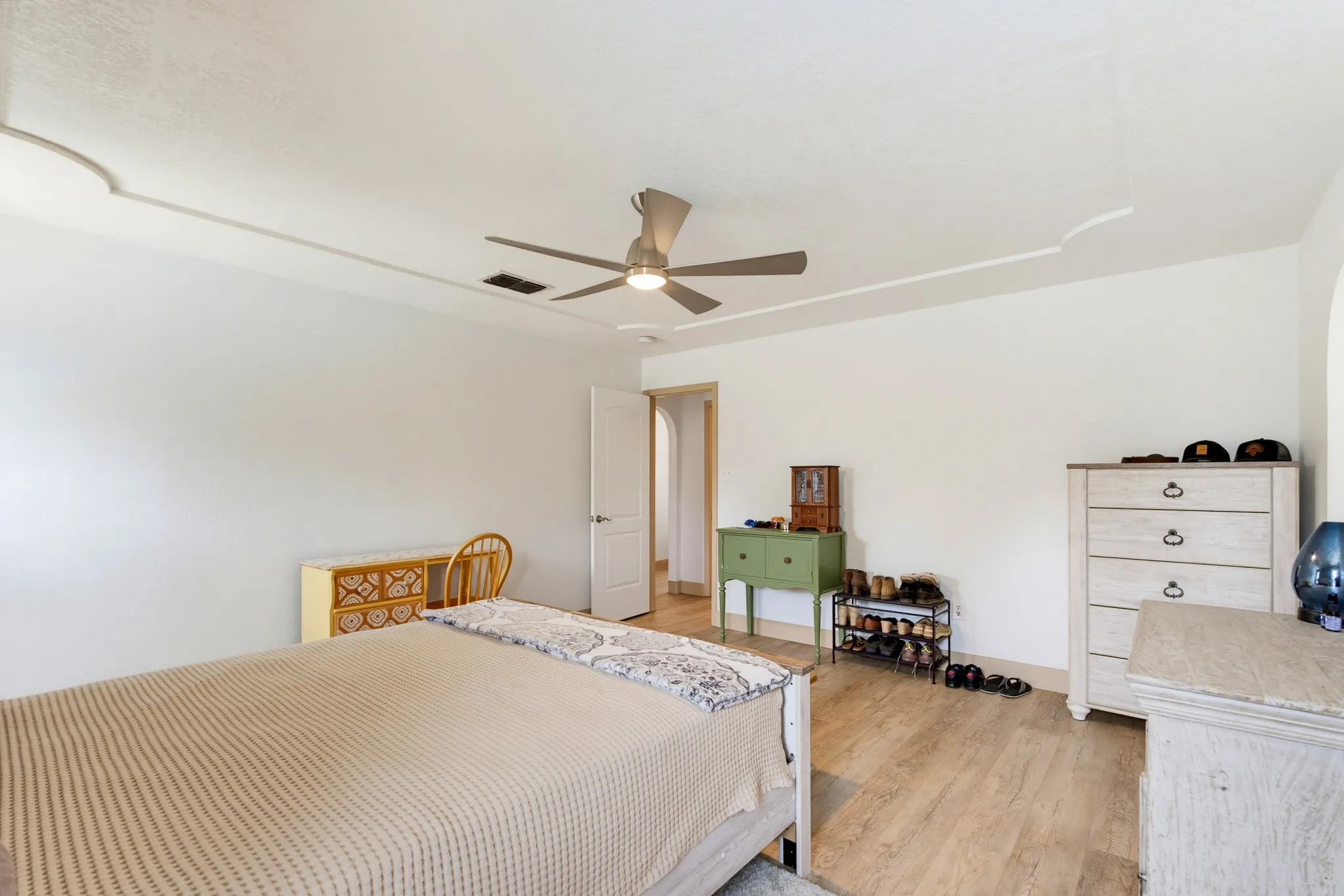 Recessed ceiling detail, ceiling fan with integrated lighting, wood-finish flooring, white walls, and a white interior door