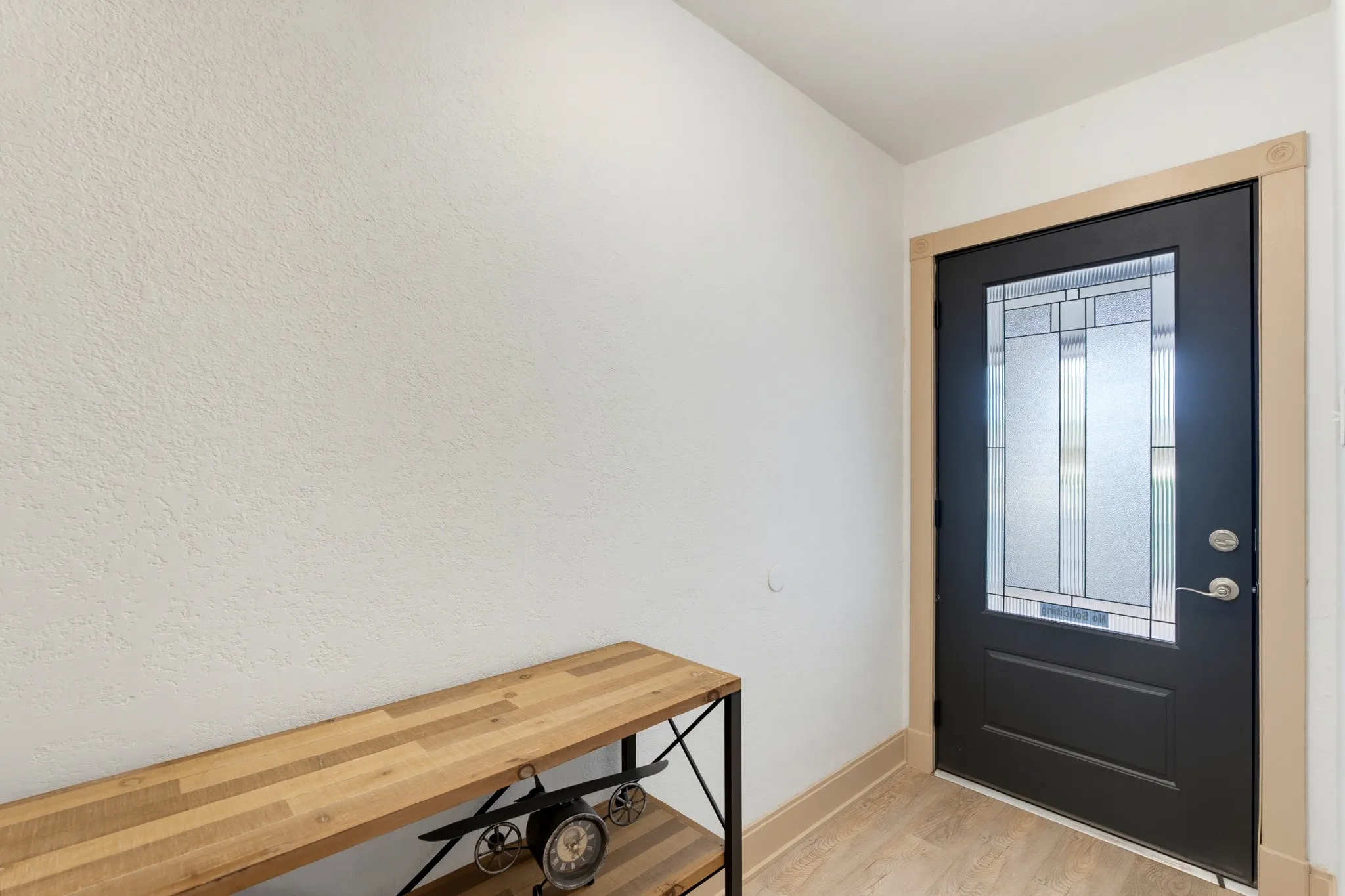 Black entry door with decorative glass panels, light wood-finish flooring, and light-toned trim