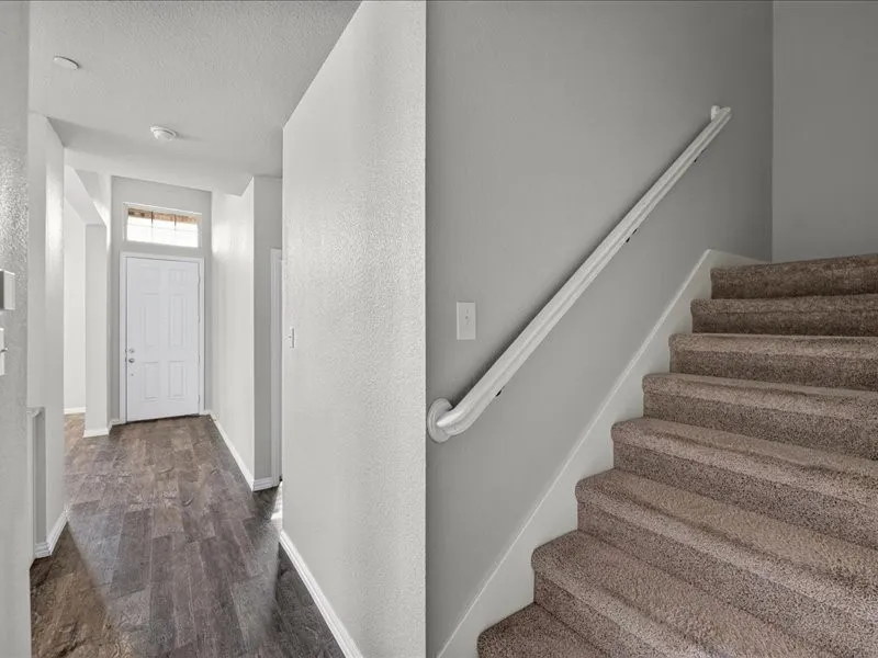 Entryway featuring wood-finish flooring, a paneled front door with transom window, and a carpeted staircase with a white handrail