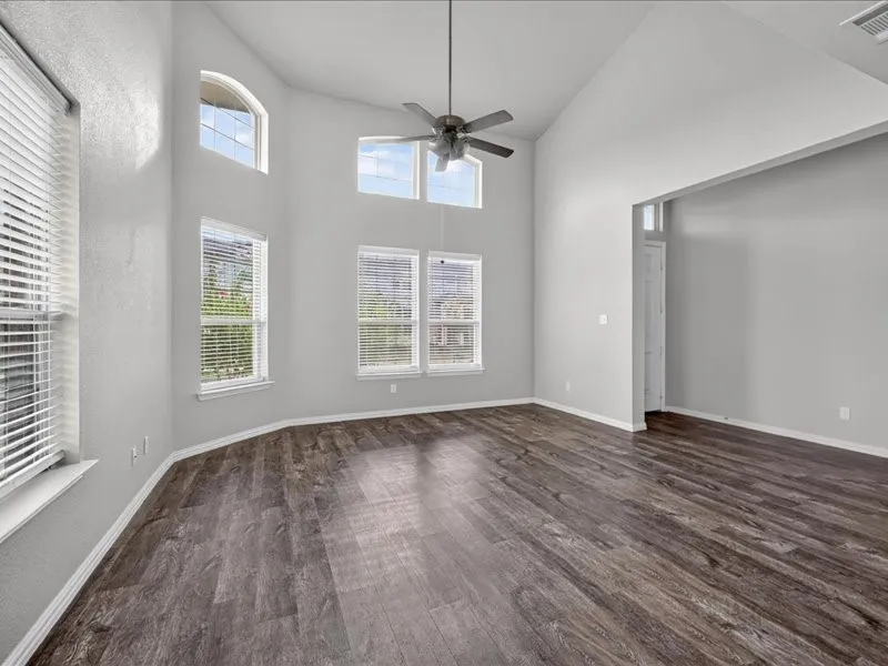 Vaulted ceiling with a ceiling fan, multiple windows, wood-finish flooring, and light-toned wall finishes