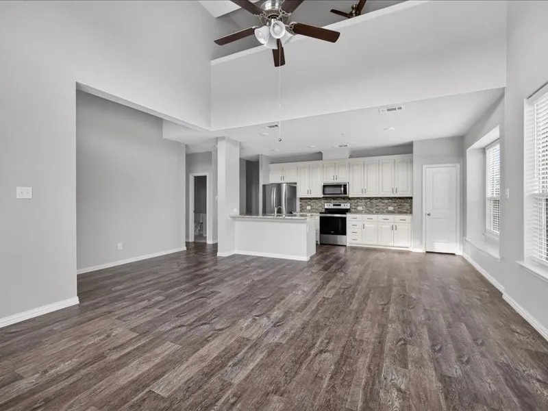Vaulted ceiling with dual ceiling fans, wood-finish flooring, white kitchen cabinetry, stainless steel appliances, and a textured tile backsplash