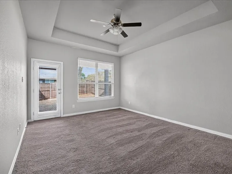 Tray ceiling with a ceiling fan, carpeted flooring, window with blinds, and a glass-paneled door