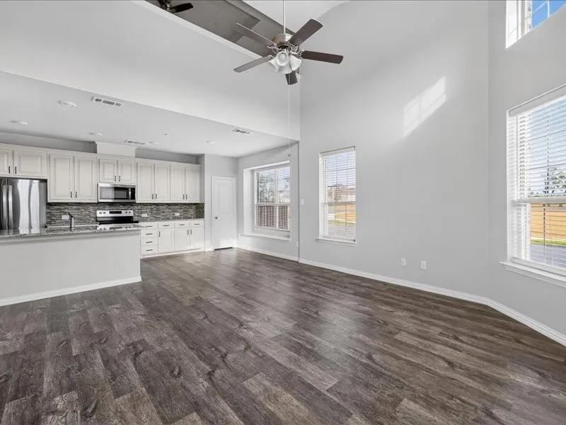 Open-concept living area featuring high vaulted ceilings, wood-finish flooring, and multiple windows with blinds
