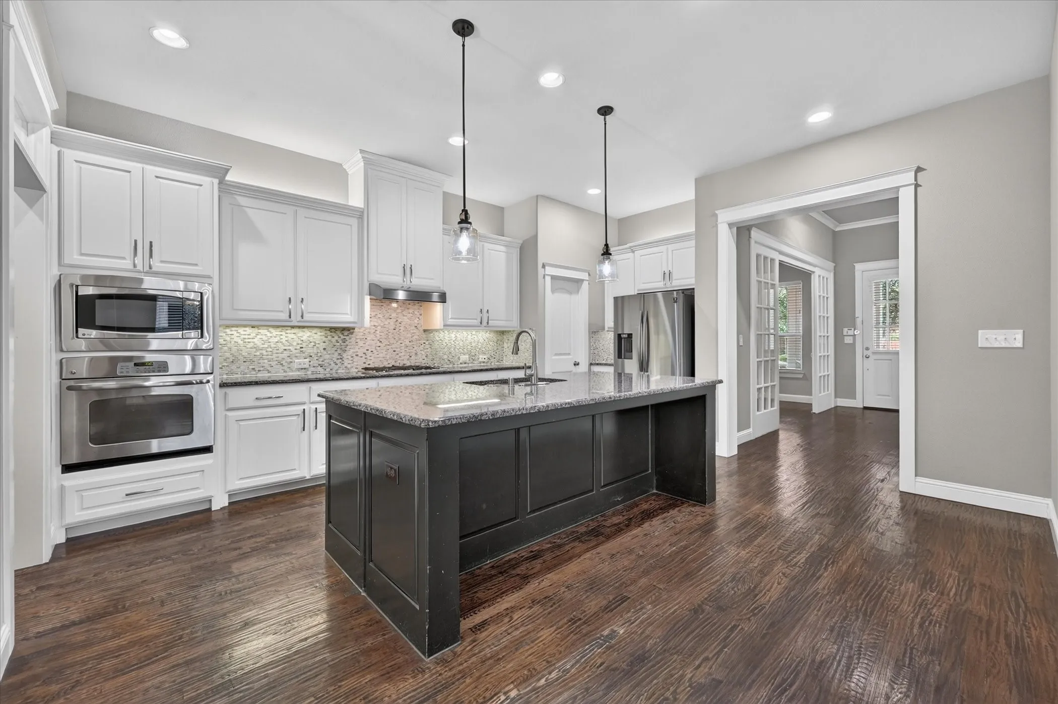 Wood-finish flooring, white cabinetry, stainless steel appliances, central island with dark cabinetry, and pendant lighting