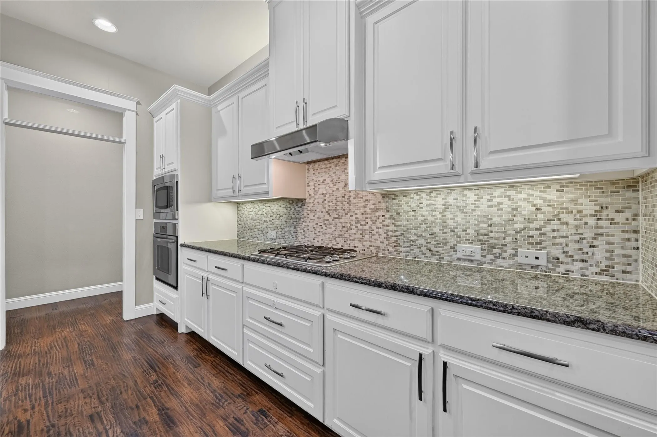 Kitchen featuring white cabinetry, dark stone countertops, mosaic tile backsplash, stainless steel appliances, and wood-finish flooring