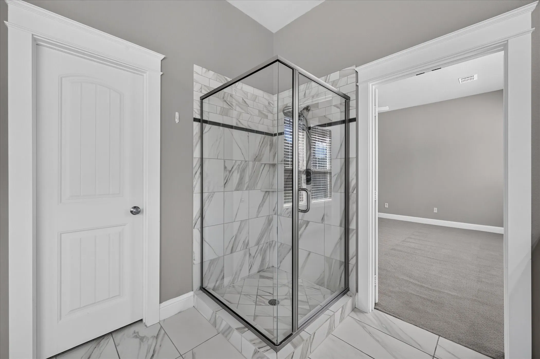 Corner glass-enclosed shower with a tiled surround, a built-in shower niche, and a window