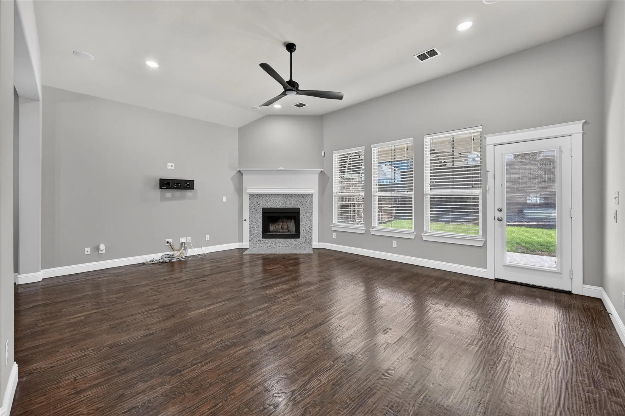 Vaulted ceiling with a ceiling fan, fireplace with a tile surround and mantle, wood-finish flooring, and multiple windows with blinds