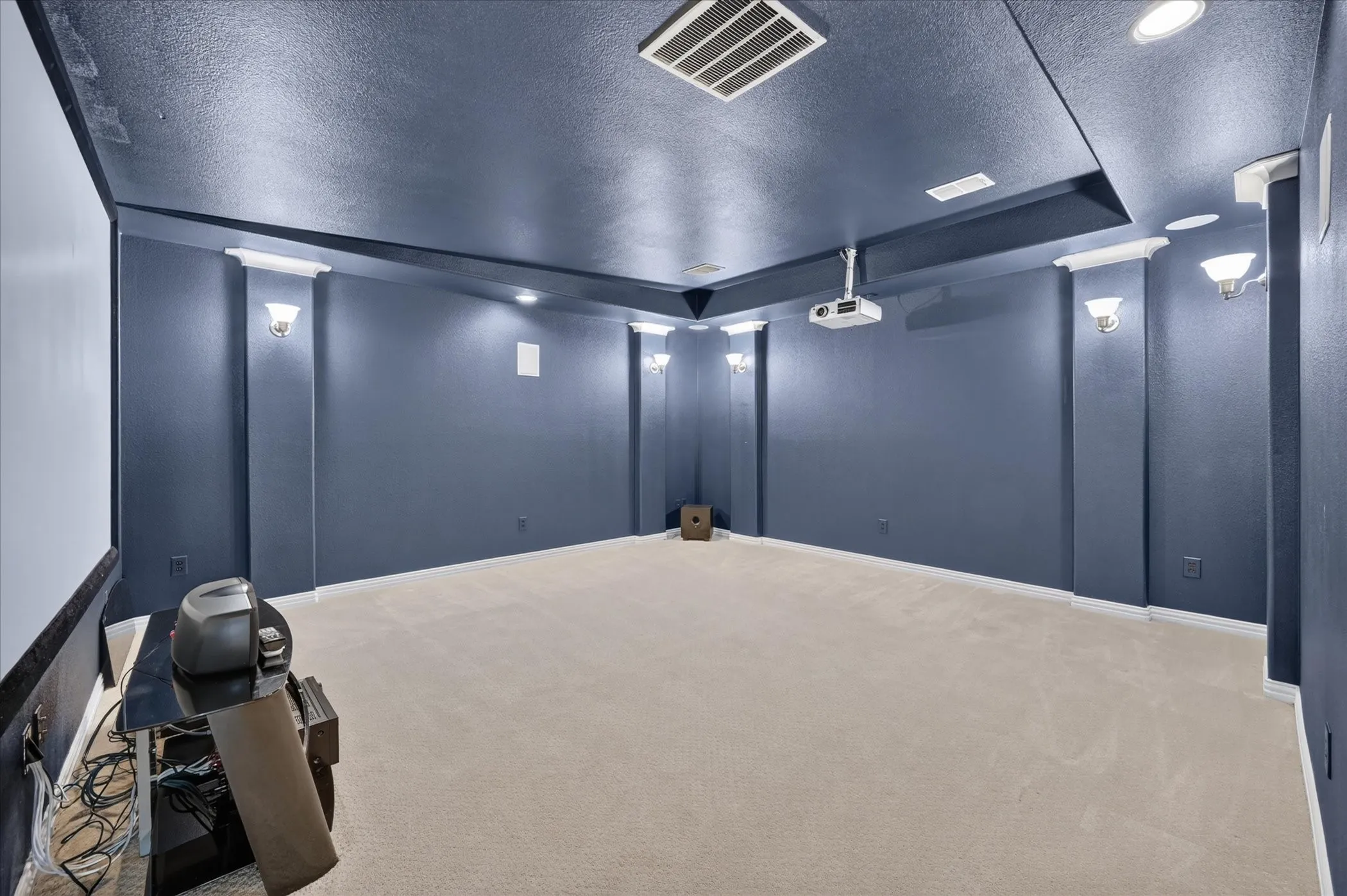 Dedicated media room featuring recessed lighting, wall sconces, ceiling-mounted projector, and a large projection screen