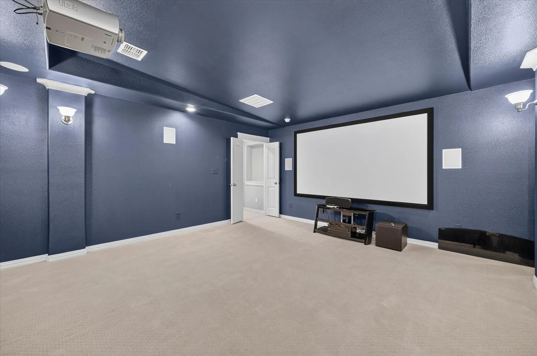 Dedicated media room featuring a large projection screen, recessed lighting, and wall-mounted sconces