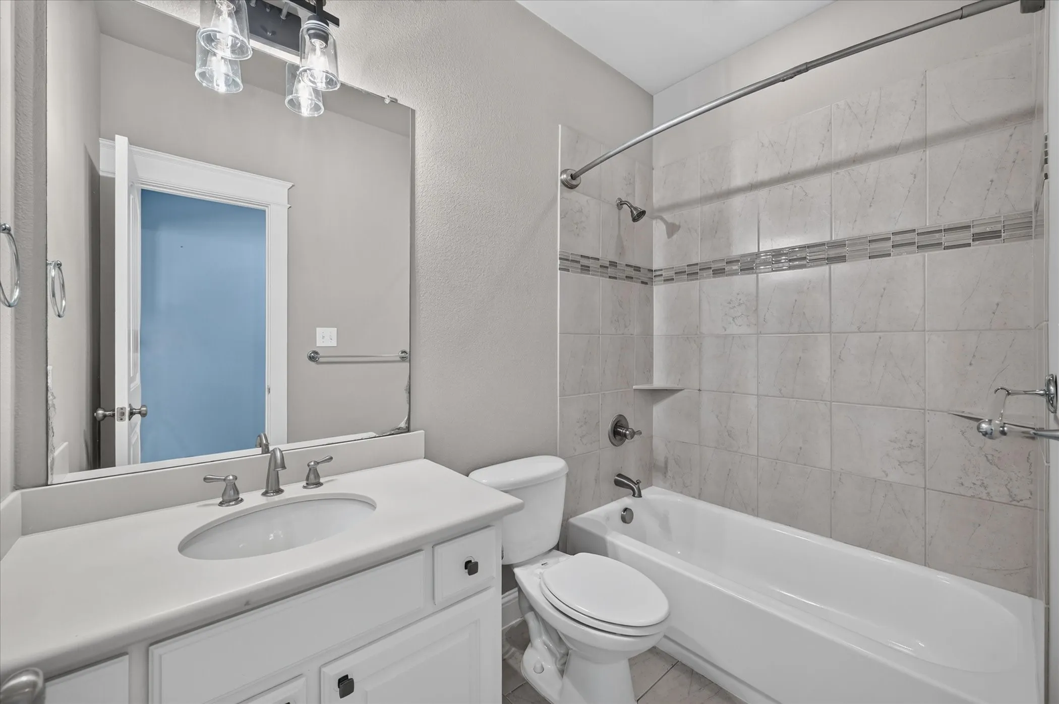 Bathroom featuring a white vanity with an integrated sink, brushed nickel fixtures, a framed mirror, and a tiled shower-tub combination with a decorative accent band