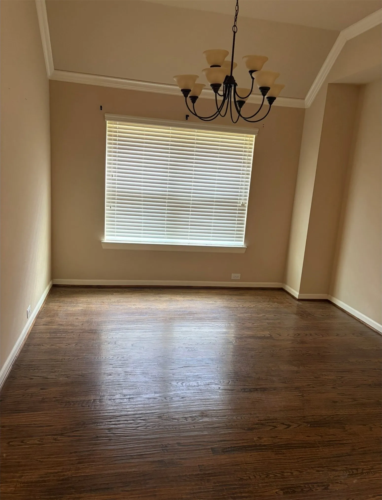 Vaulted ceiling with crown molding, elegant chandelier, expansive window, and rich wood-finish flooring