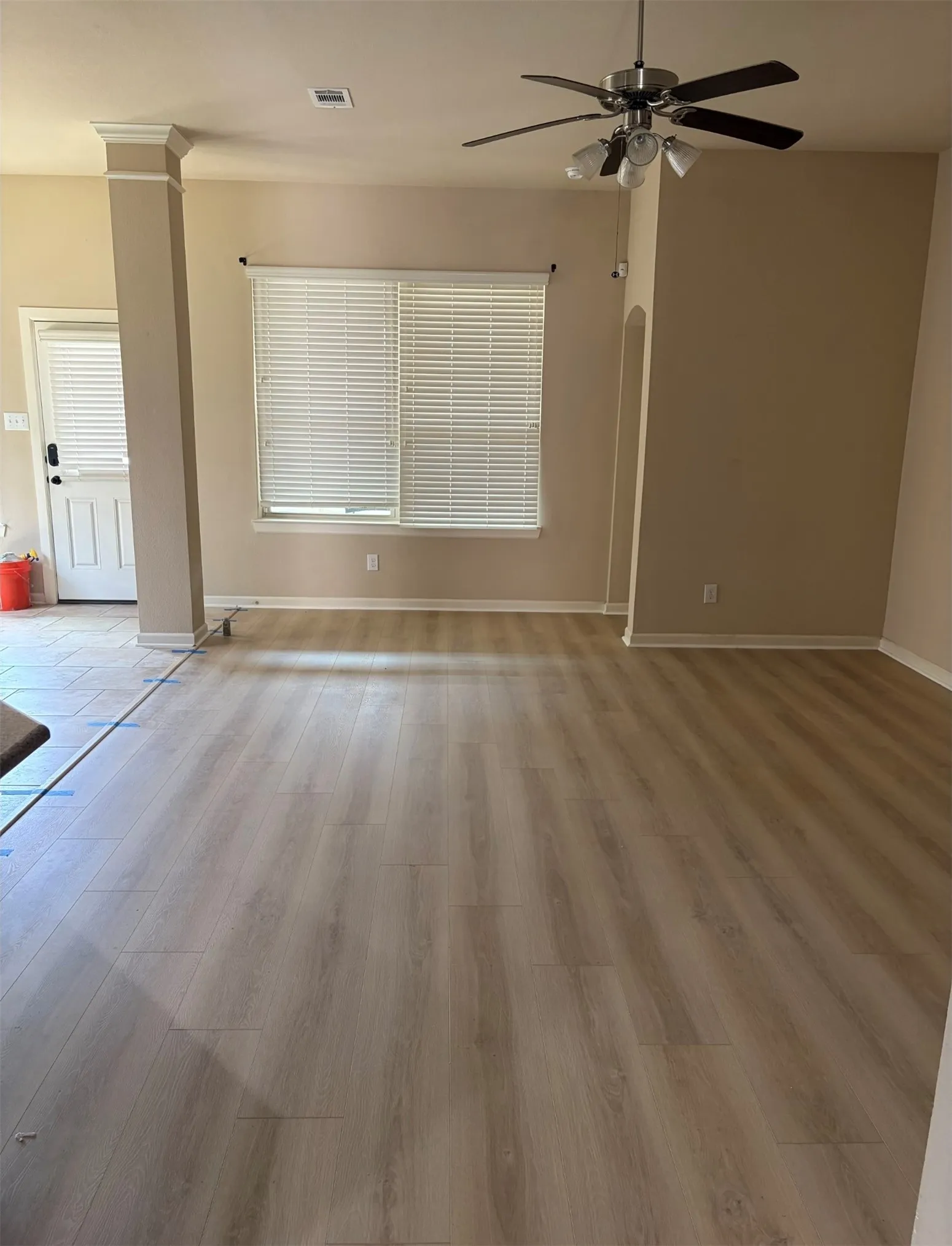 Wood-finish flooring throughout, ceiling fan with integrated lighting, window with horizontal blinds, and an arched doorway