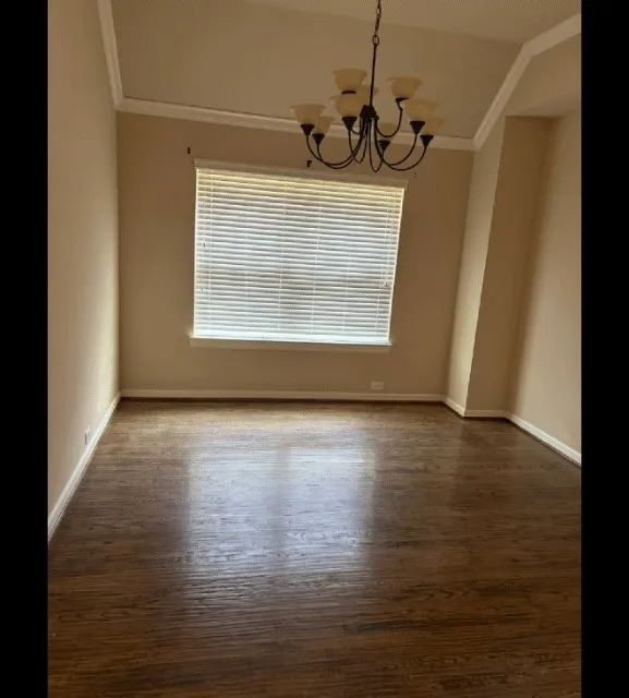 Wood-finish flooring, tray ceiling with crown molding, and a multi-arm chandelier