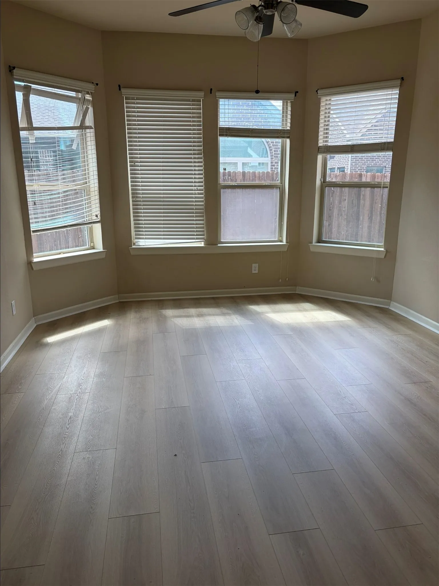 Bay window with multiple windows, wood-finish flooring, and a ceiling fan with integrated lighting
