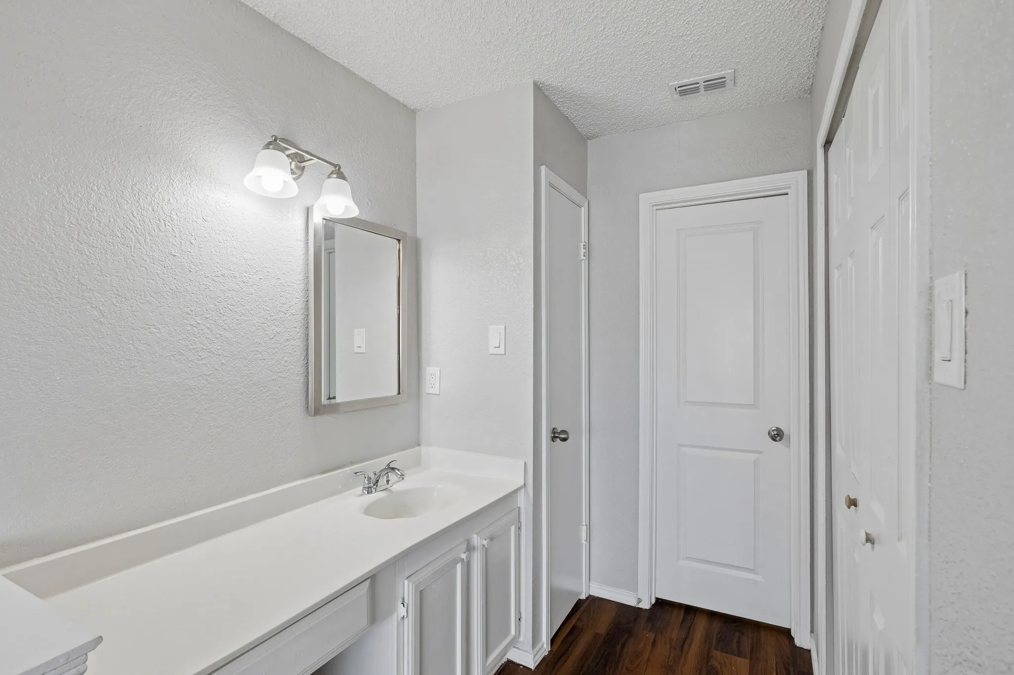 Single vanity with integrated sink, white cabinetry, and wood-finish flooring