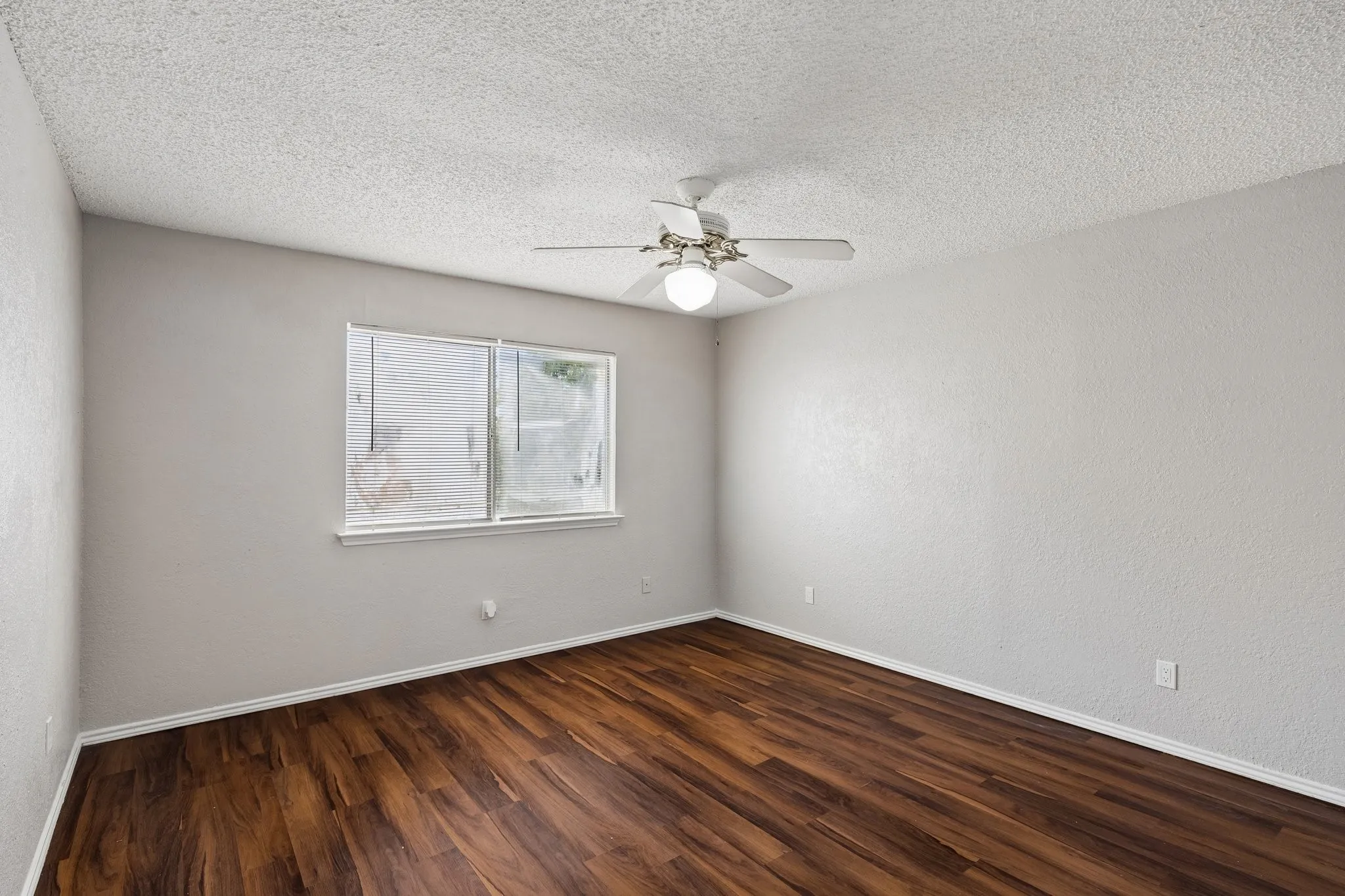 Wood-finish flooring, neutral wall tones, ceiling fan with integrated lighting, and a window for natural illumination